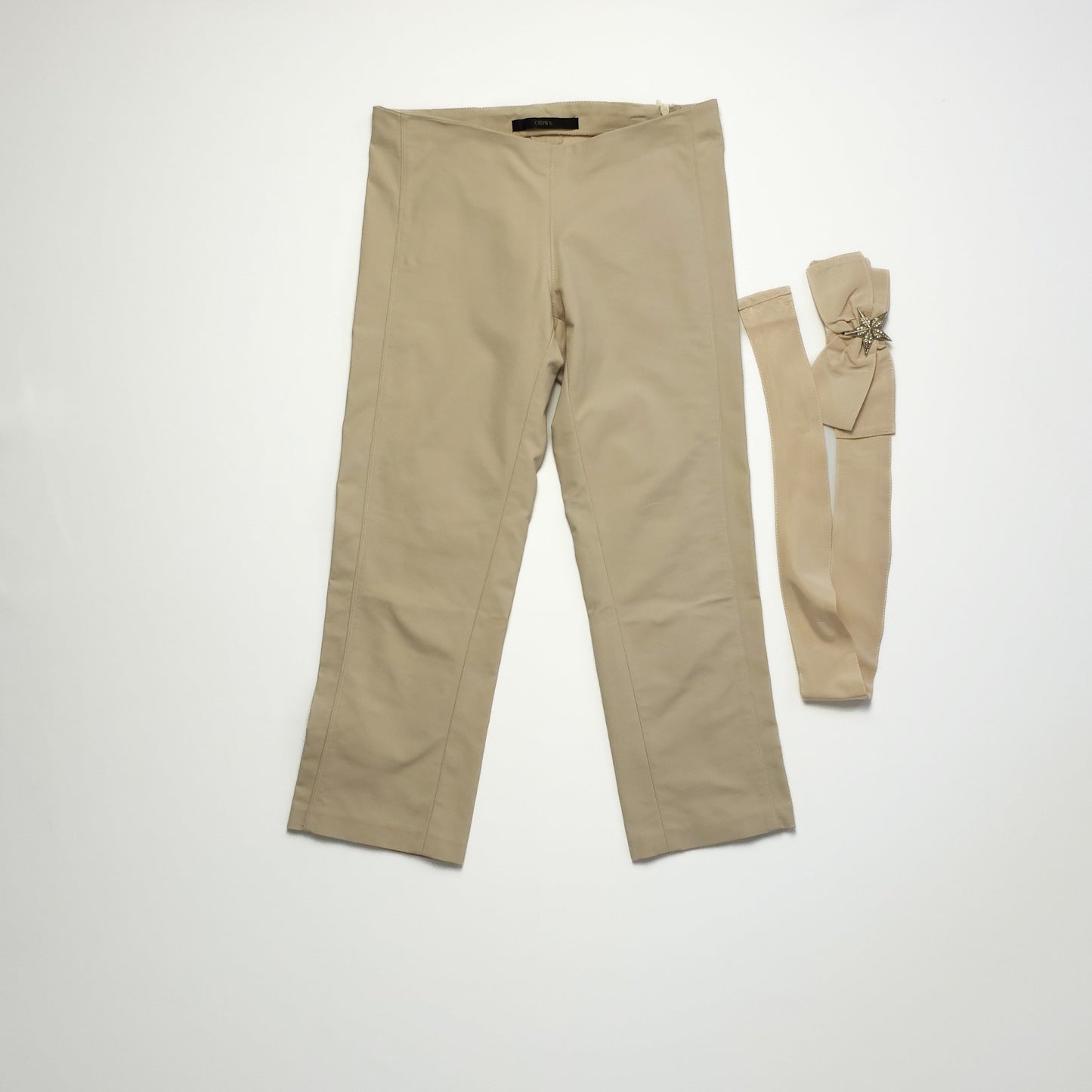 Beige women's pants with a matching fabric belt featuring a bow detail laid beside them on a light background.