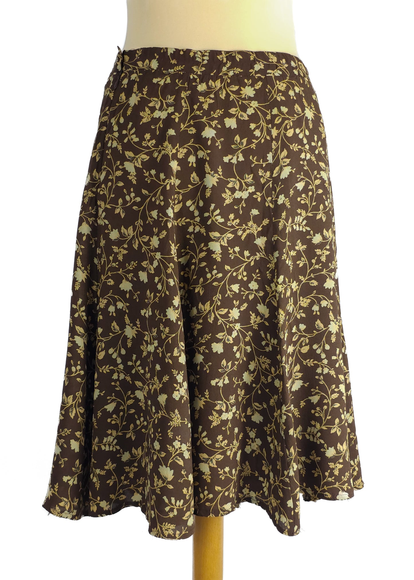 Brown A-line skirt with a cream floral print on a mannequin, showcasing a knee-length design with a gentle flare and subtle pleats.