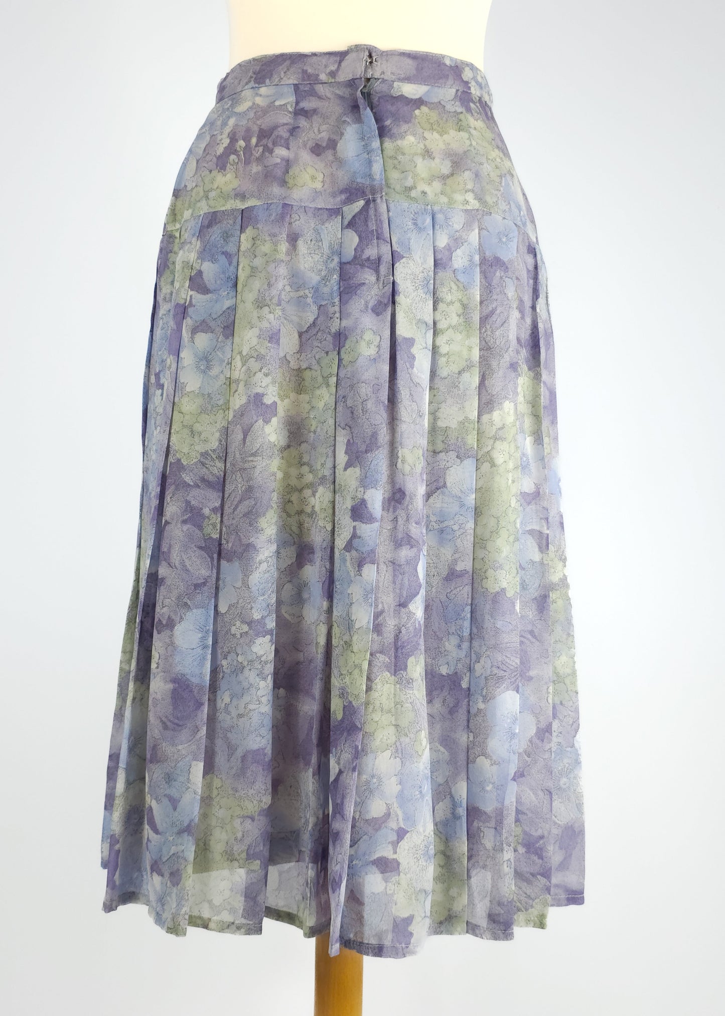 A pleated, midi-length skirt with a floral pattern in shades of blue, green, and lavender. The skirt has a fitted waistband and a subtle back zipper.