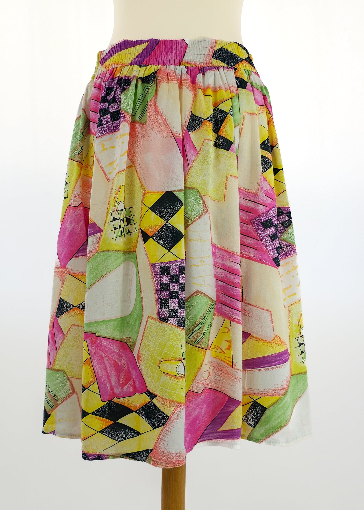 A colorful knee-length skirt with an elastic waistband, featuring a vibrant geometric pattern in pink, yellow, green, and black on a white background.