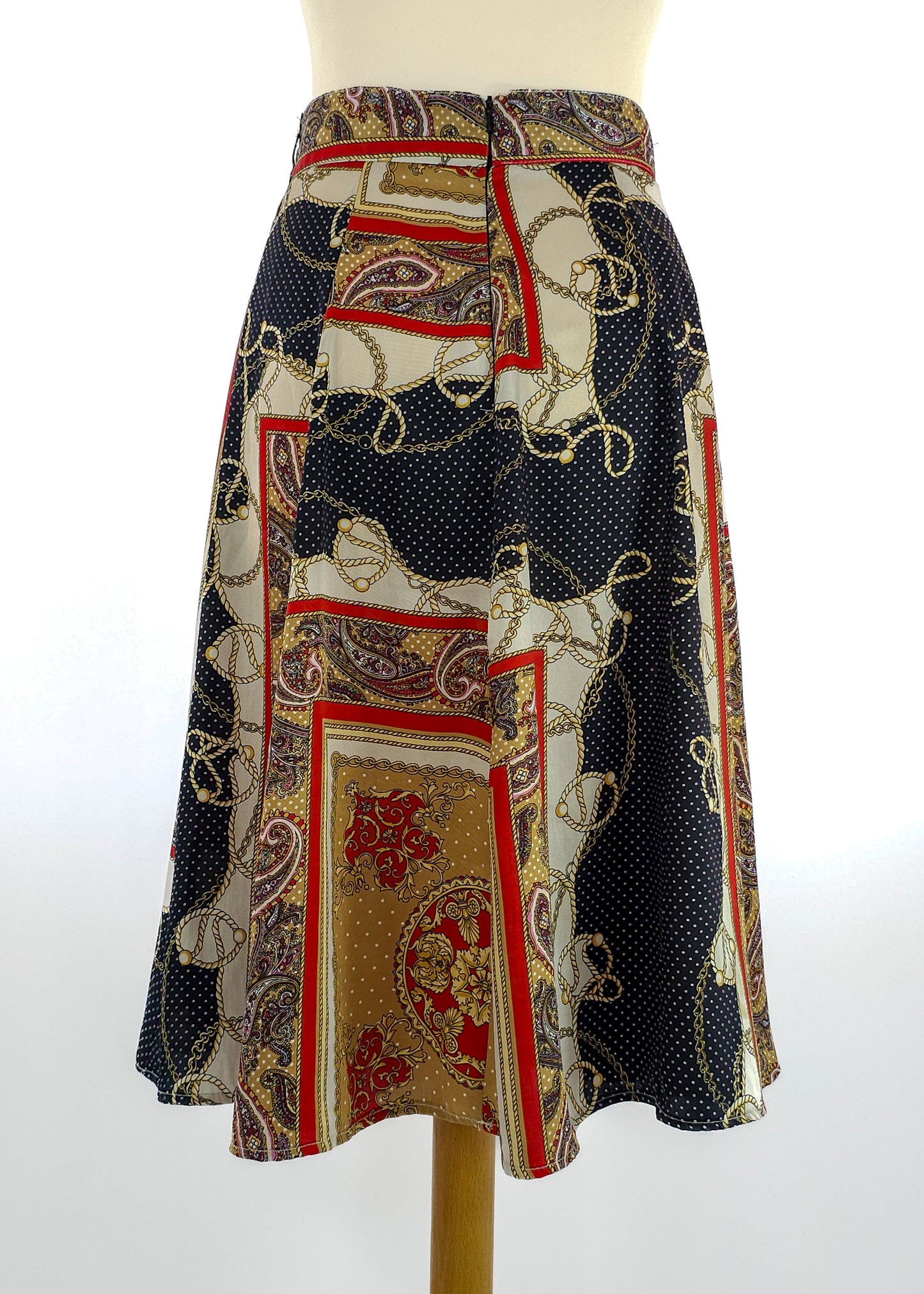 A vintage A-line skirt with a paisley and polka dot pattern in black, red, and gold. It features a high waist and a knee-length hem.