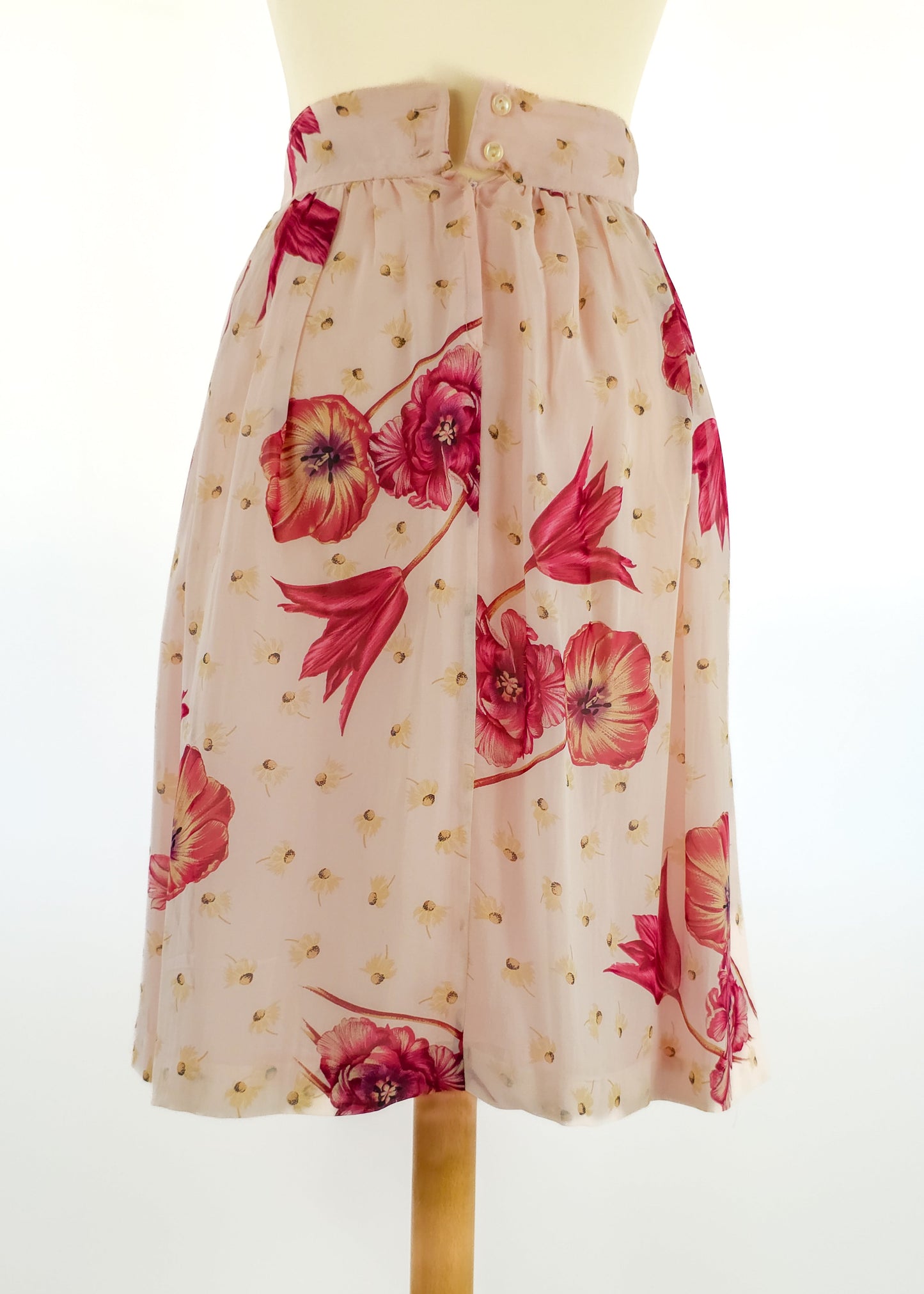 Pink floral knee-length skirt with red and yellow flowers and a buttoned waistband displayed on a mannequin against a plain white background.