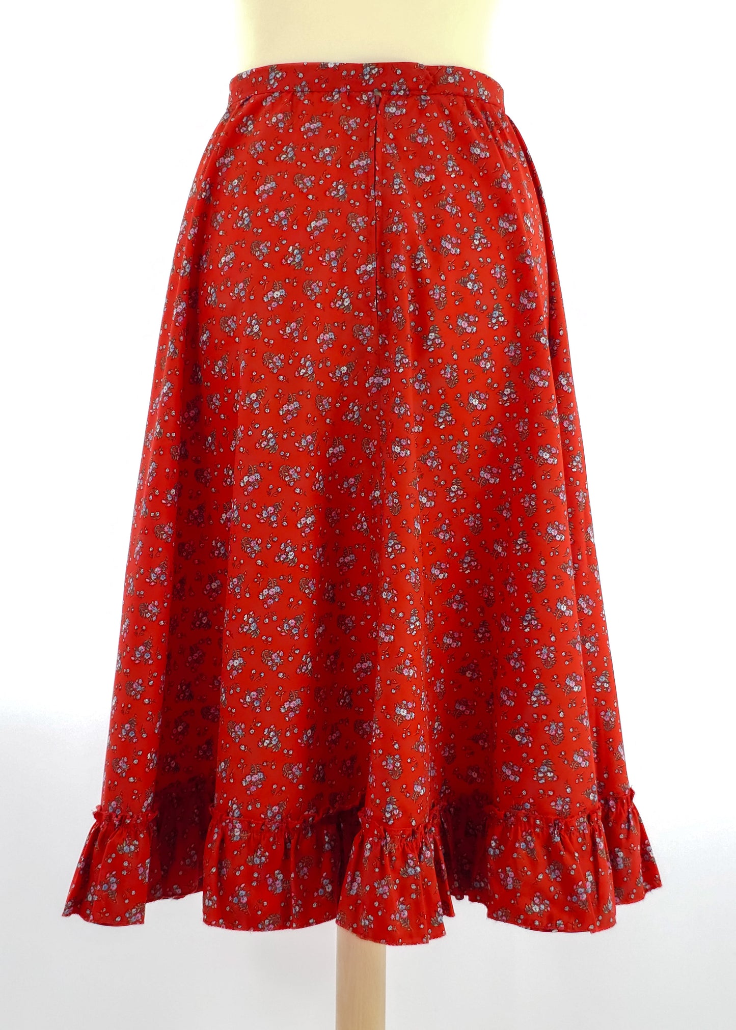 A red floral midi skirt with a ruffled hem displayed on a mannequin. The skirt features a small white and blue floral pattern and an A-line silhouette.