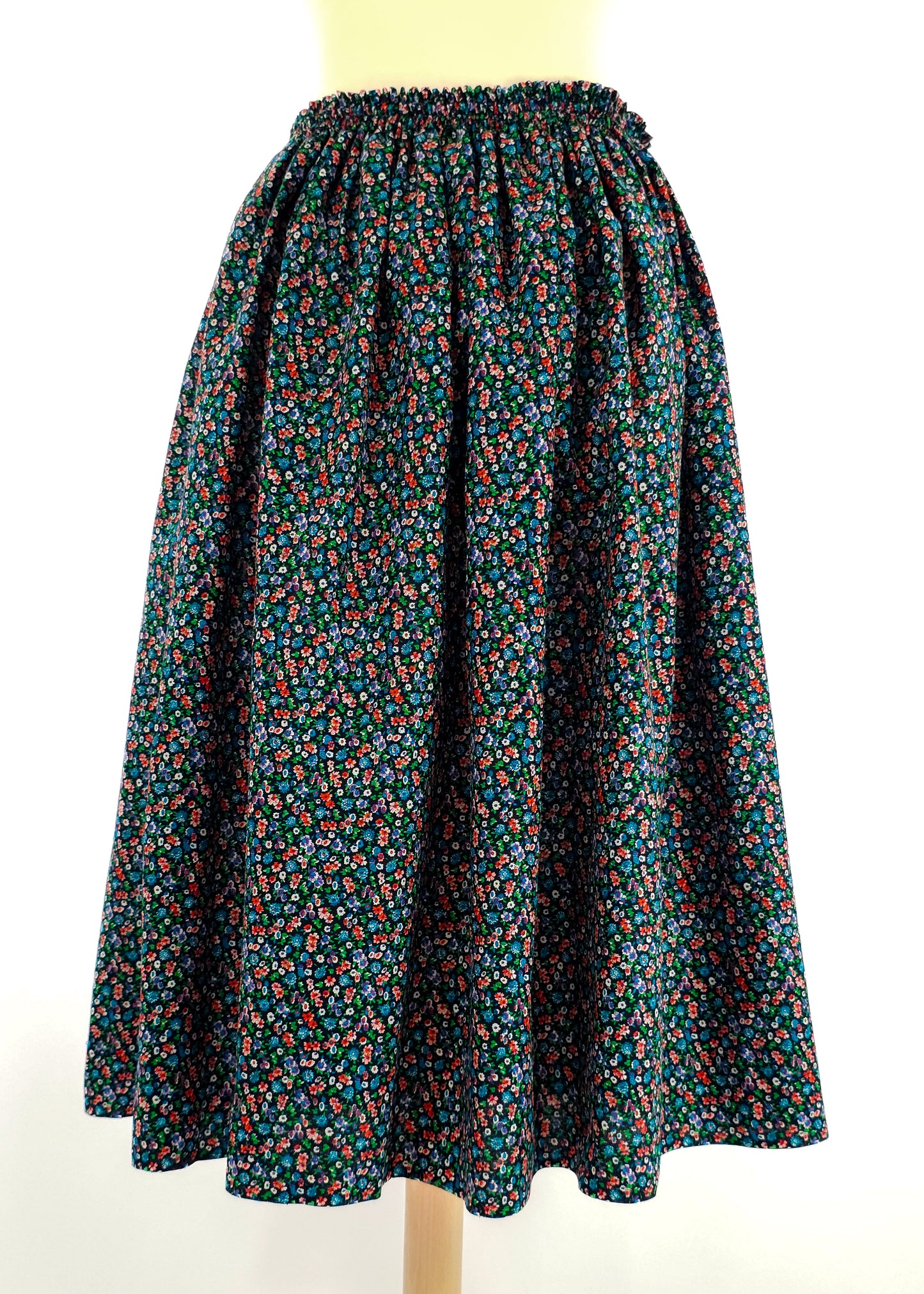 A long, flowing skirt with a colorful floral pattern on a dark background, featuring an elastic waistband. The skirt is displayed on a mannequin.