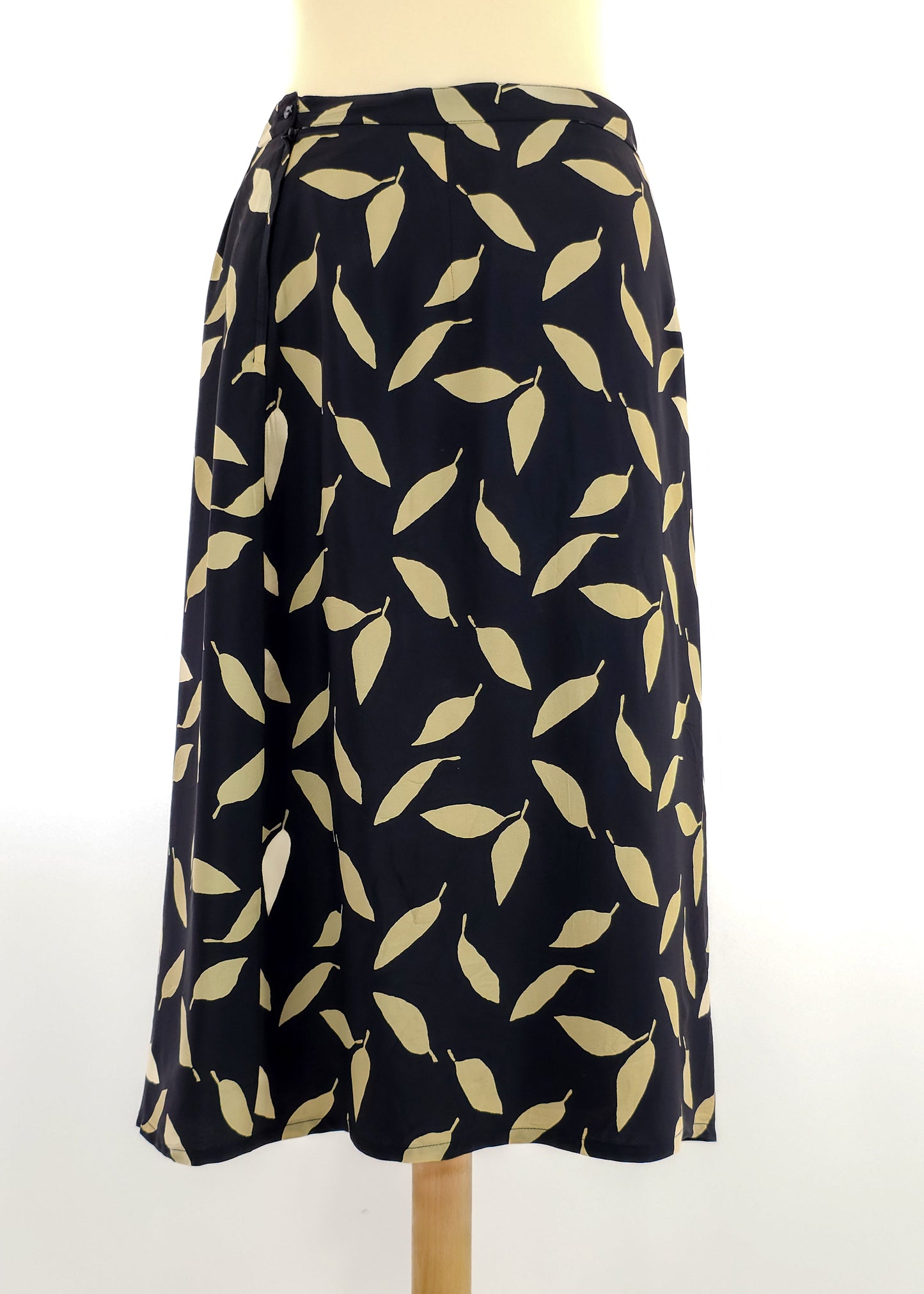 A knee-length black skirt with a wrap design featuring a beige leaf pattern, displayed on a mannequin against a plain white background.