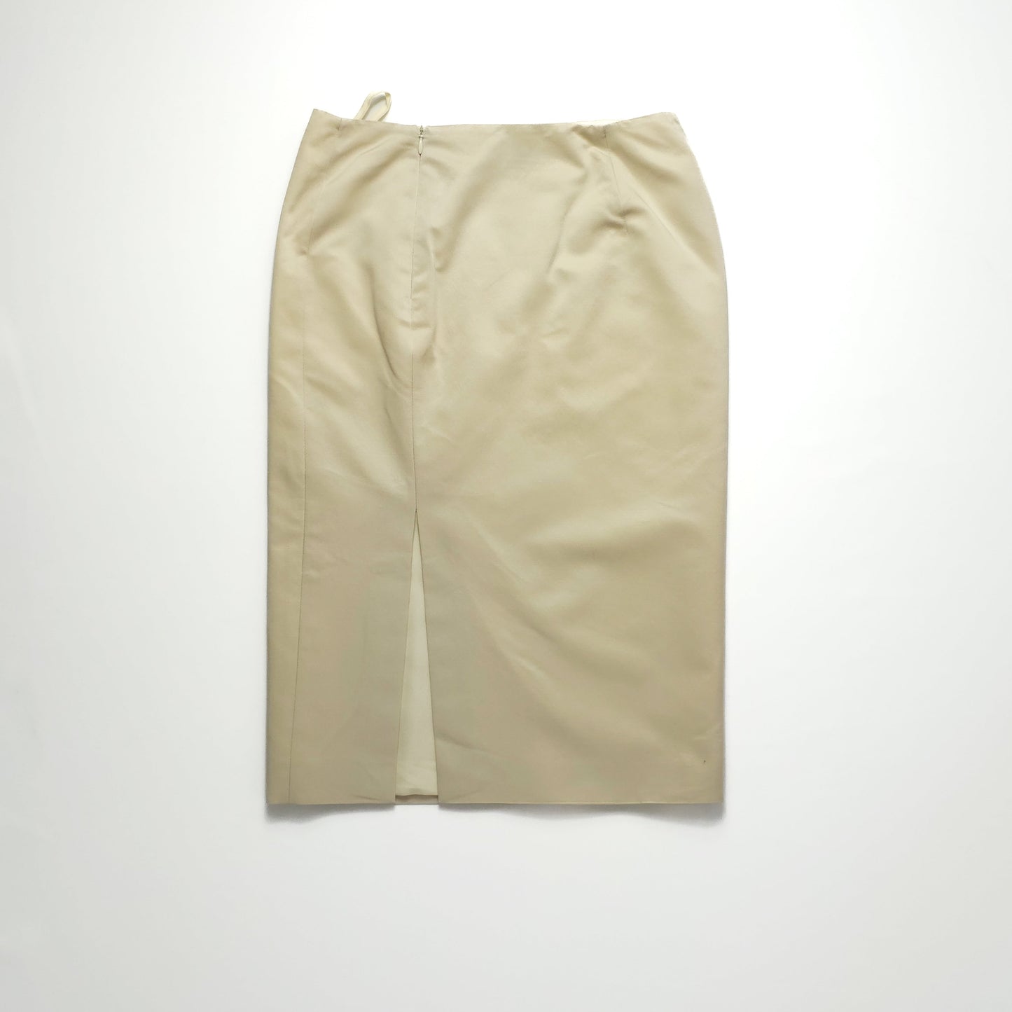 Beige pencil skirt with a high waist and a back slit, displayed on a plain light background. Skirt features subtle seam details and a tailored fit.