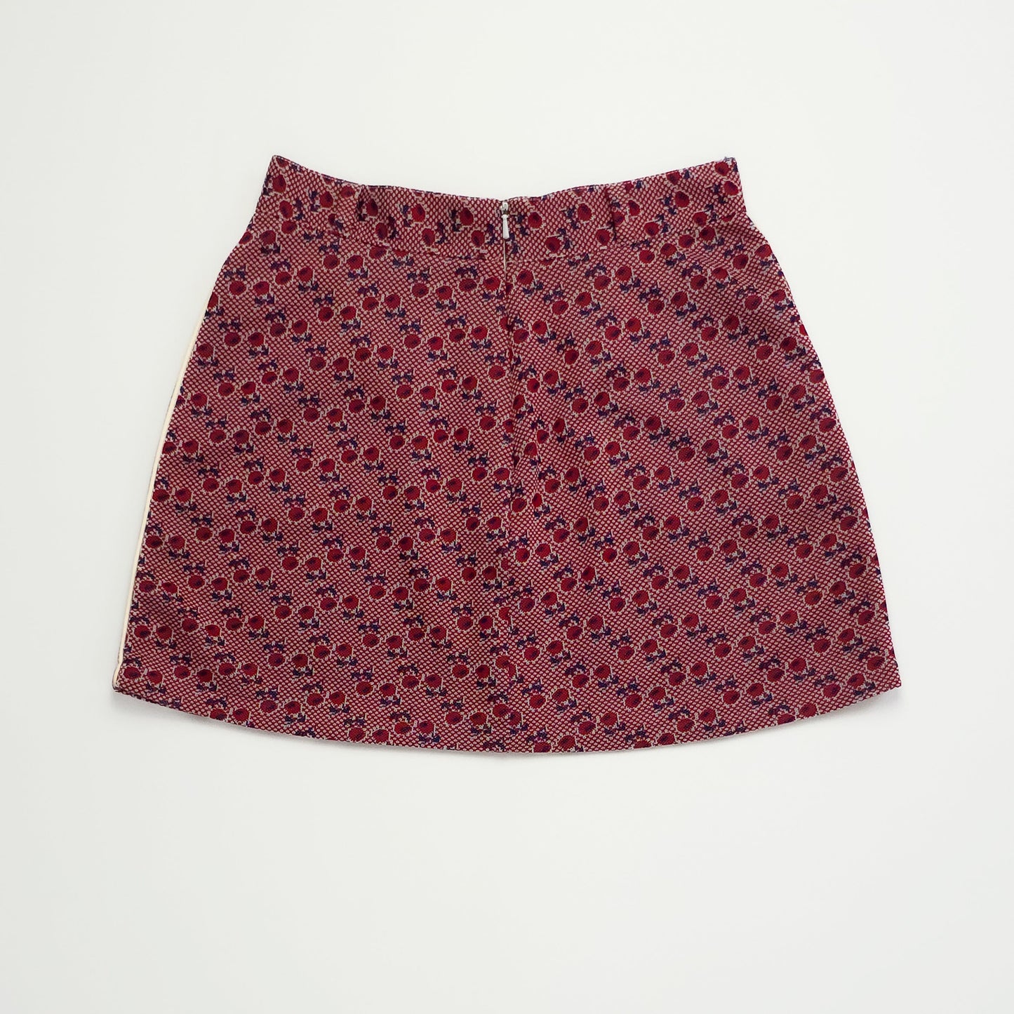 A vintage A-line skirt with a geometric pattern in red and brown shades, featuring textured fabric and a side zipper, displayed against a plain white background.