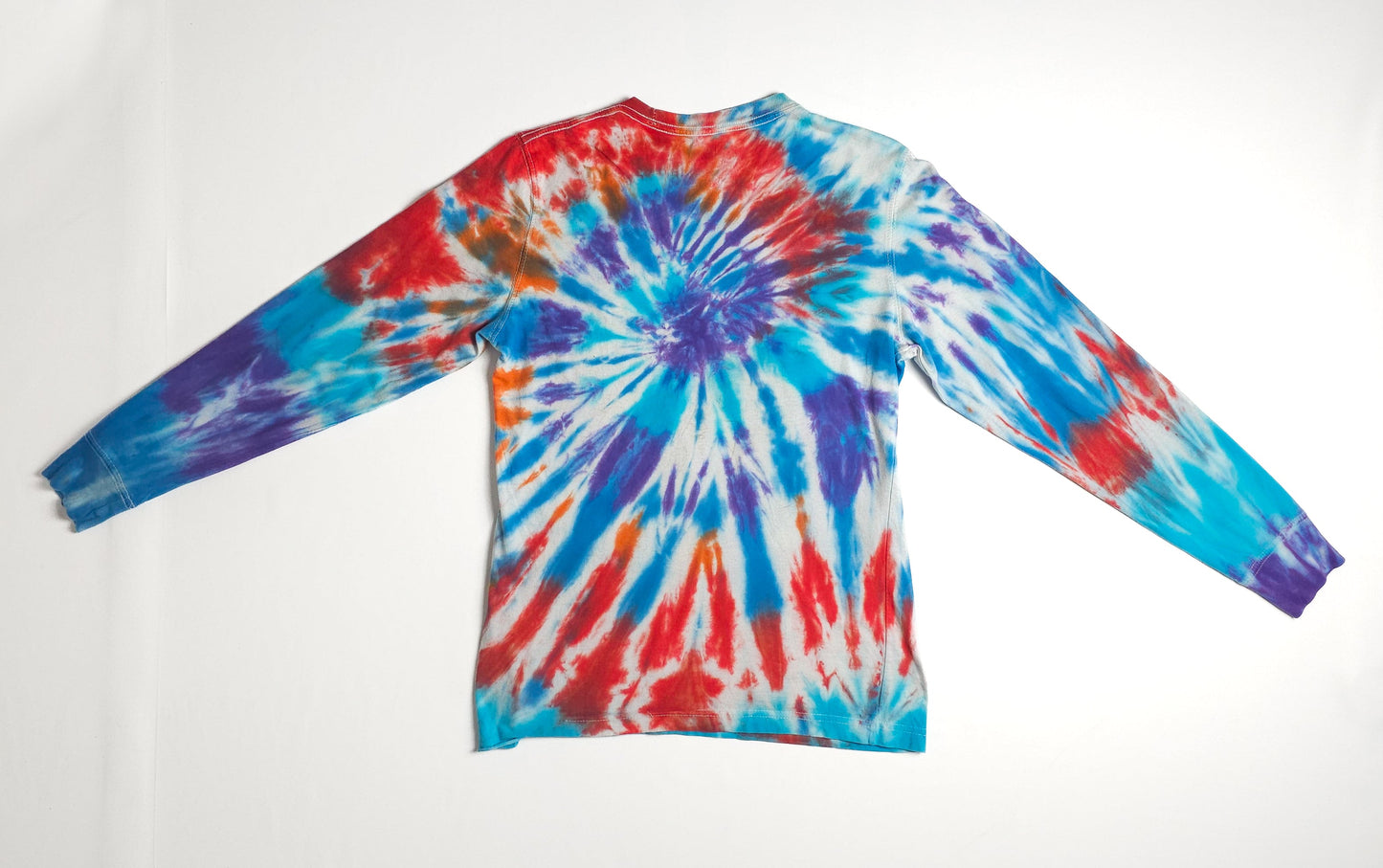 A vibrant long-sleeve tie-dye shirt with a spiral pattern in red, blue, purple, and turquoise on a white background, laid flat on a white surface.