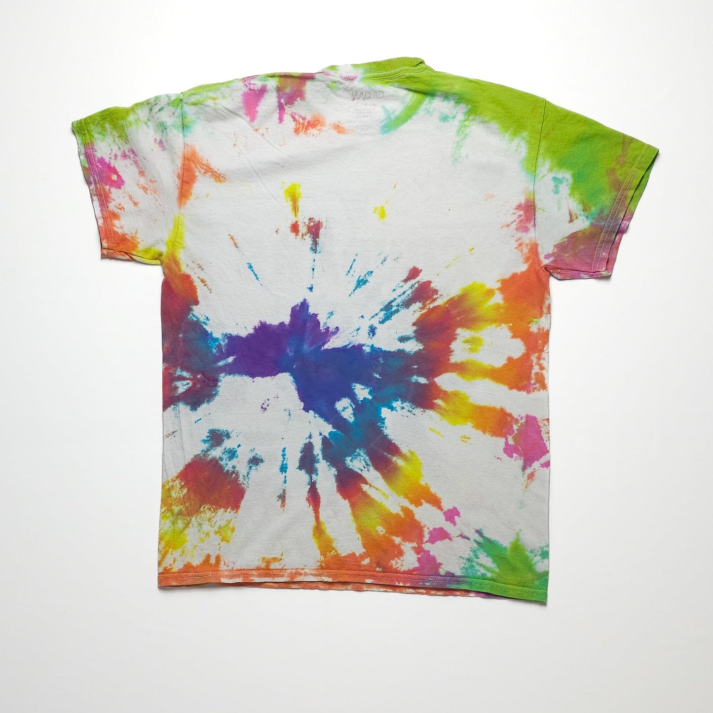 A colorful tie-dye T-shirt with a splatter pattern featuring shades of green, orange, purple, and blue against a white background, displayed on a flat surface.