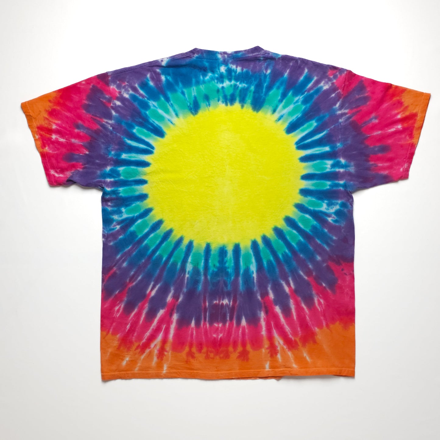 A vibrant tie-dye t-shirt with a bold yellow center surrounded by blue, pink, purple, and red rings, creating a sunburst pattern. The bottom edge is orange.