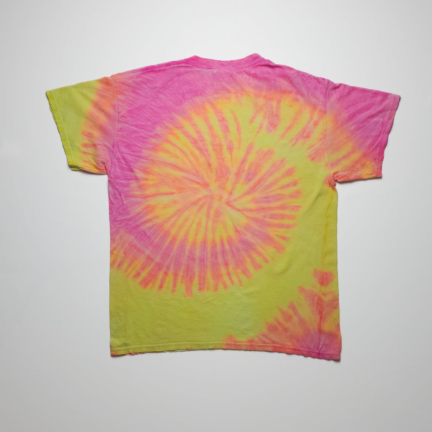 A vibrant tie-dye t-shirt with a spiral pattern in pink and yellow hues, displayed flat on a plain background. The shirt has short sleeves and a round neckline.