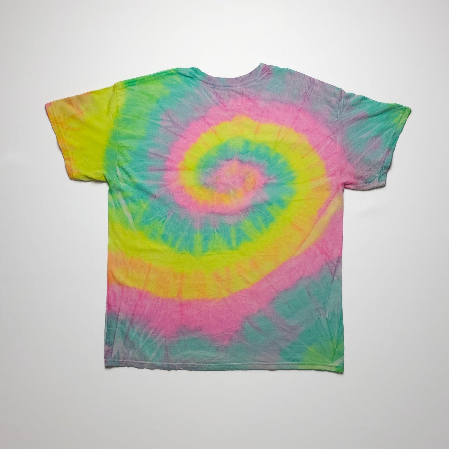 Colorful tie-dye T-shirt featuring a spiral design with vibrant pink, yellow, blue, and green hues, laid flat on a plain background.