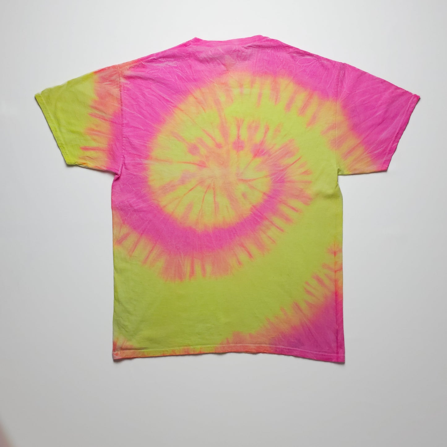 A vibrant tie-dye t-shirt with a bright pink and yellow spiral design on a light background, laid flat on a plain surface.