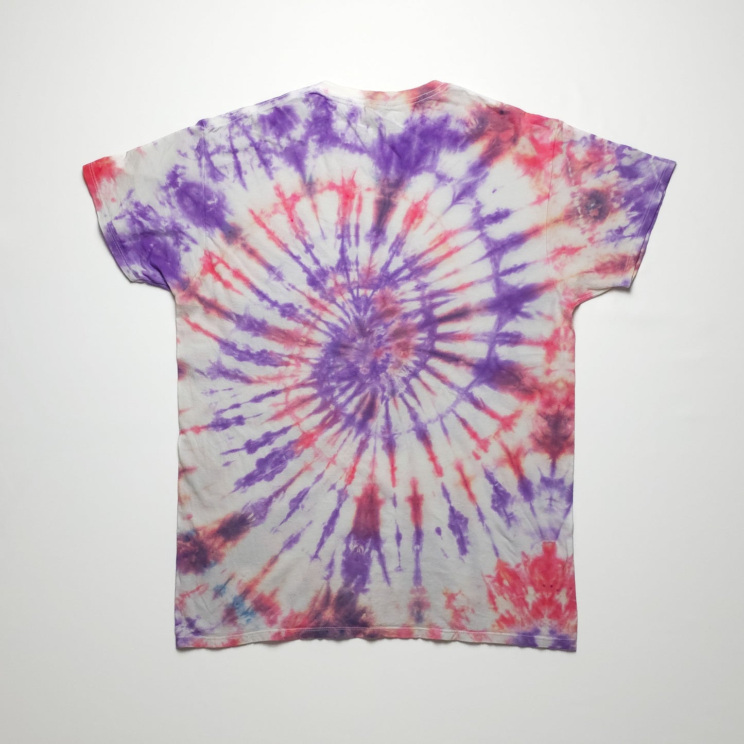 A tie-dye t-shirt with a spiral pattern in purple, red, and white hues, showcasing a vibrant and colorful design on a short-sleeved cotton fabric.