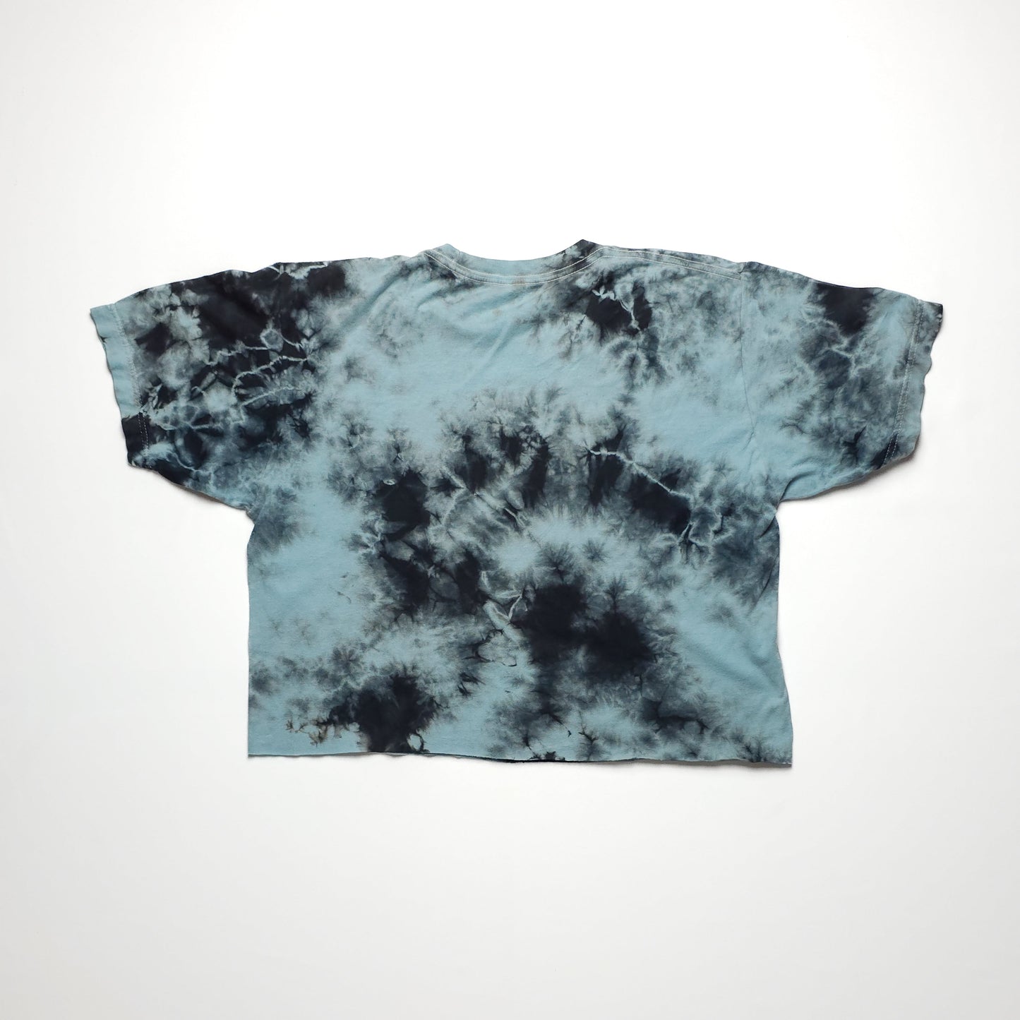 A blue tie-dye t-shirt with black and white patterns, featuring short sleeves and a relaxed fit, laid flat on a white background.