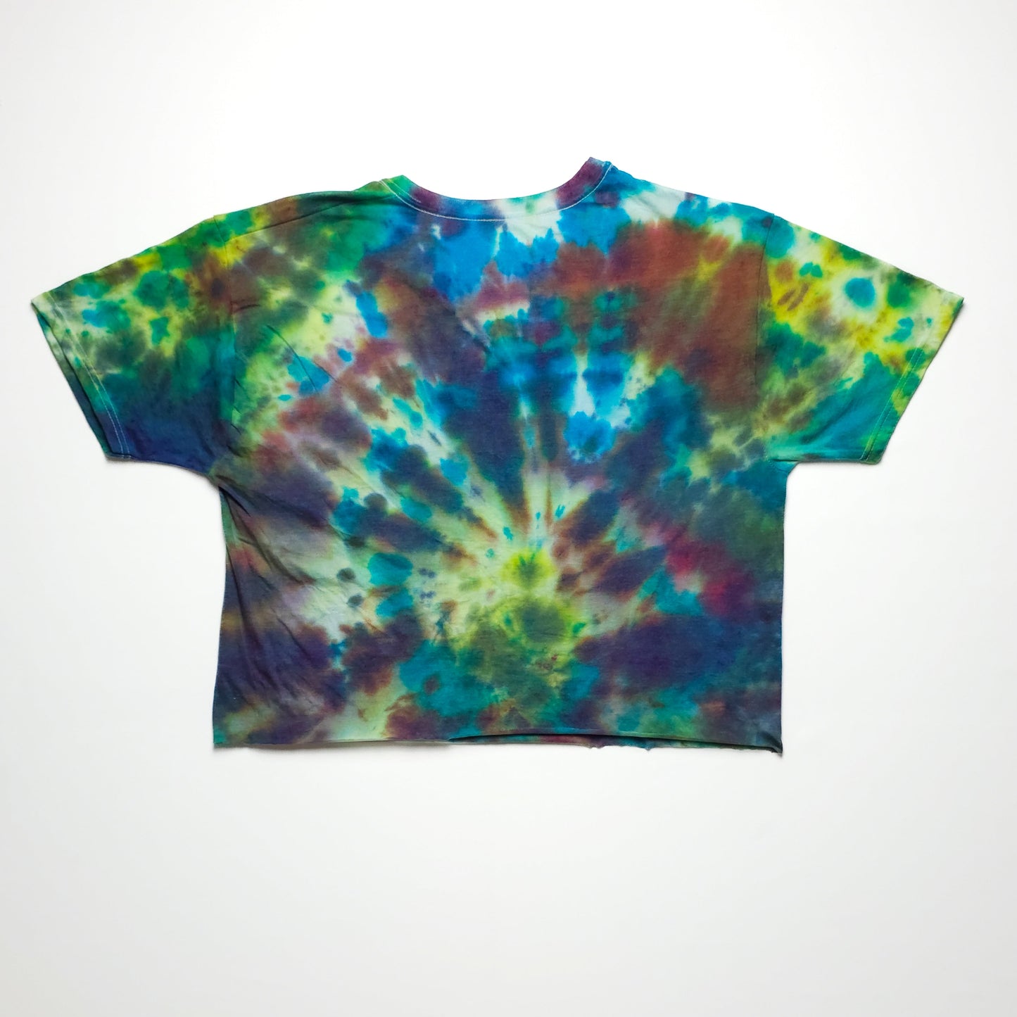 A vibrant tie-dye t-shirt with a spiral pattern in shades of blue, green, yellow, and red, spread on a flat surface. The shirt has short sleeves.