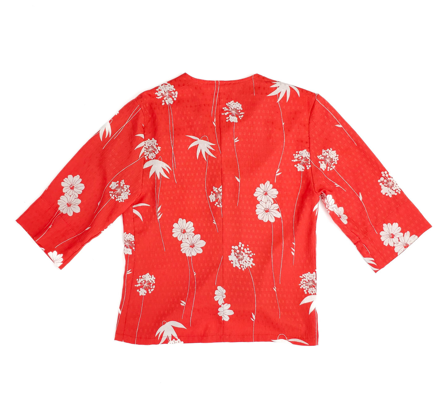 Red floral patterned blouse with three-quarter sleeves, featuring white flowers and leaves. The blouse has a straight hem and no visible buttons or zippers.