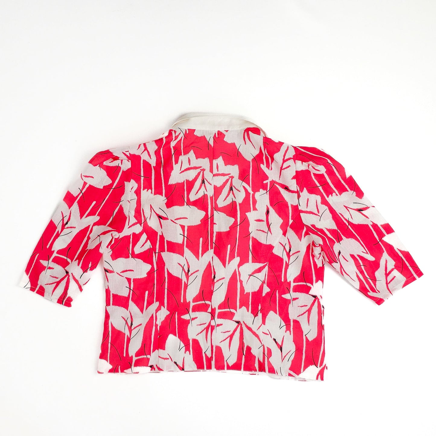 Red and white vintage blouse with a bold leaf pattern and three-quarter sleeves, displayed on a flat surface.