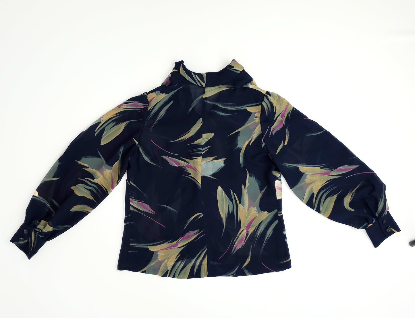 A long-sleeve blouse with an abstract feather print in green, yellow, and pink on a black background, featuring a high collar and buttoned cuffs.