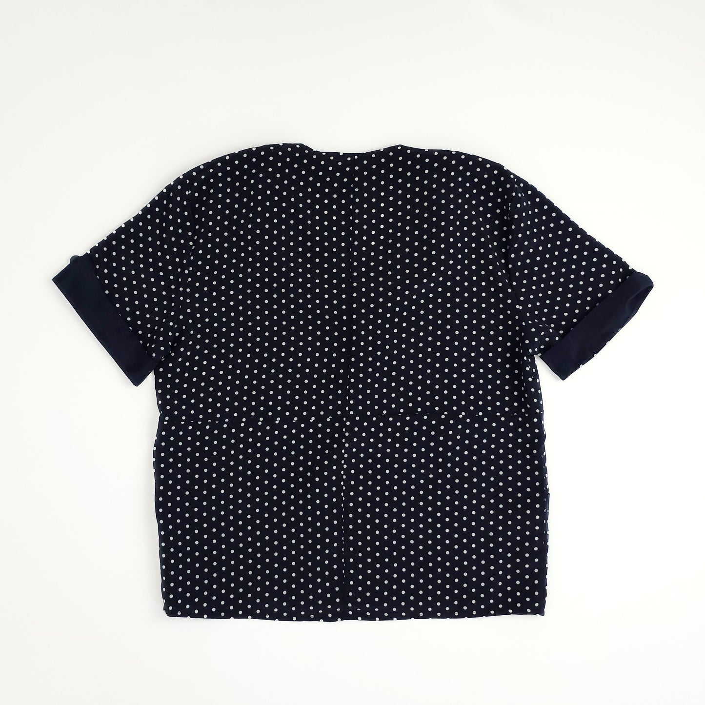 Black blouse with white polka dots, featuring short sleeves and a loose fit, displayed on a flat surface.