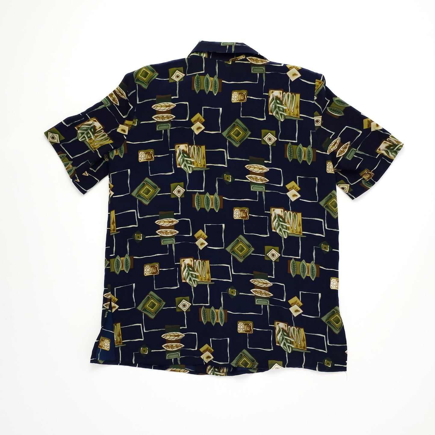 A short-sleeved shirt with a geometric and abstract pattern in green, beige, and gold on a dark blue background, displayed flat from the back.
