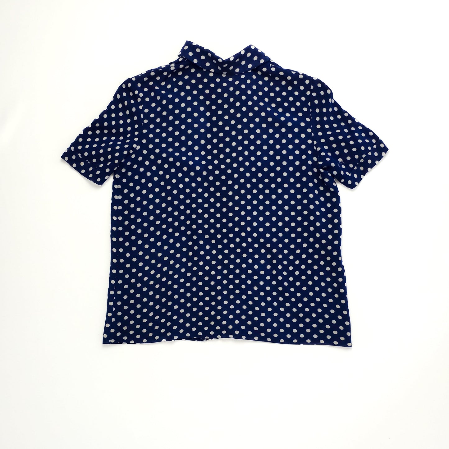 Navy blue short-sleeve blouse with white polka dots, displayed flat, showcasing its classic and casual design.