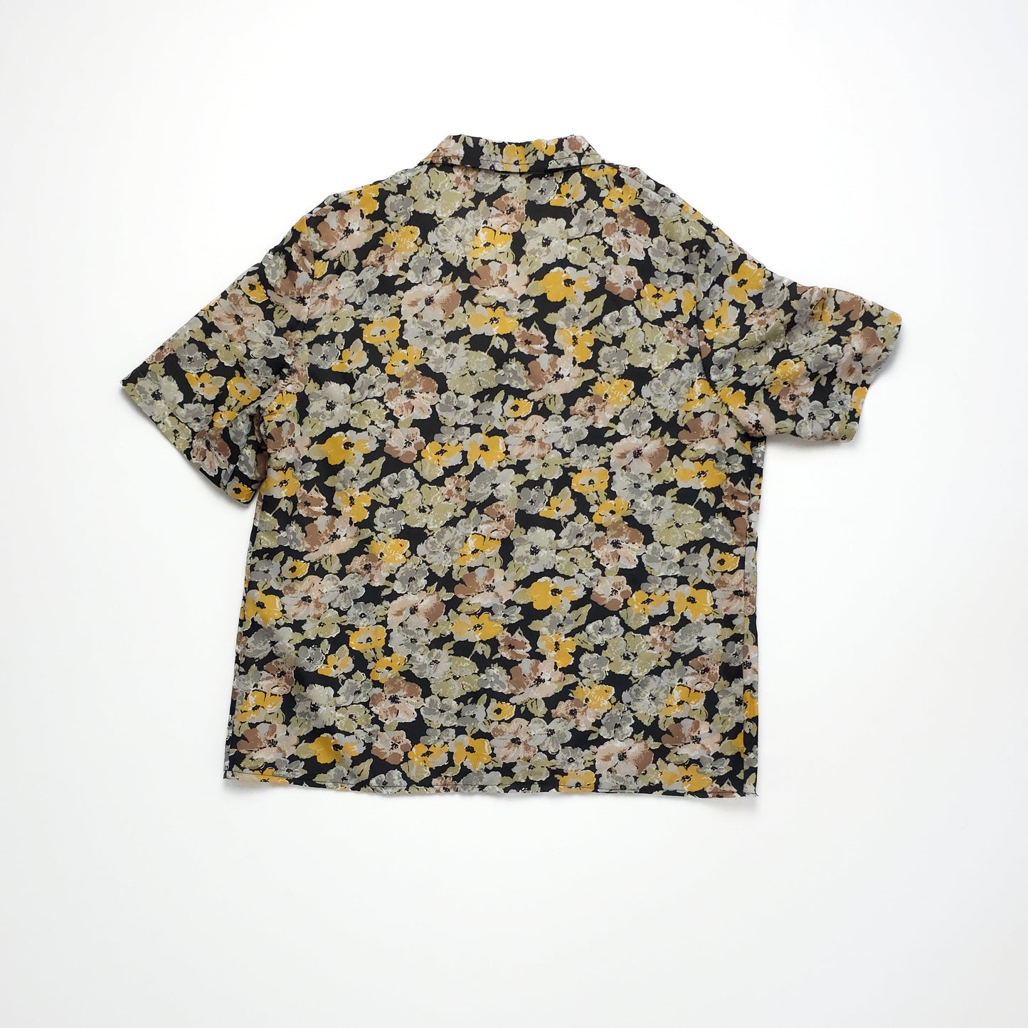 A short-sleeved, floral-patterned blouse in shades of beige, yellow, and green on a black background. The blouse has a relaxed fit and a round neck.