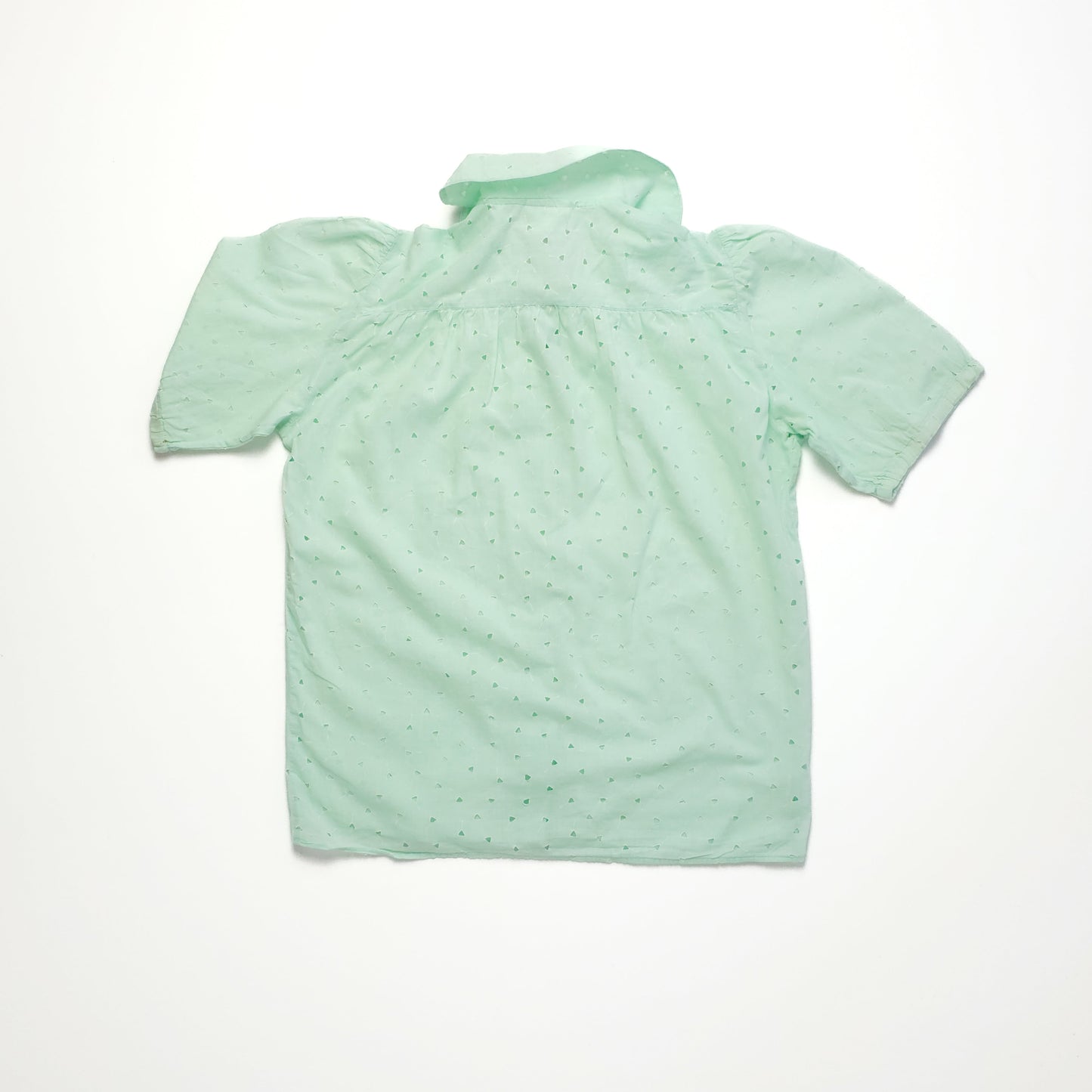Light green short-sleeve blouse with subtle dot pattern, featuring a relaxed collar and gathered back detail, laid flat on a white background.