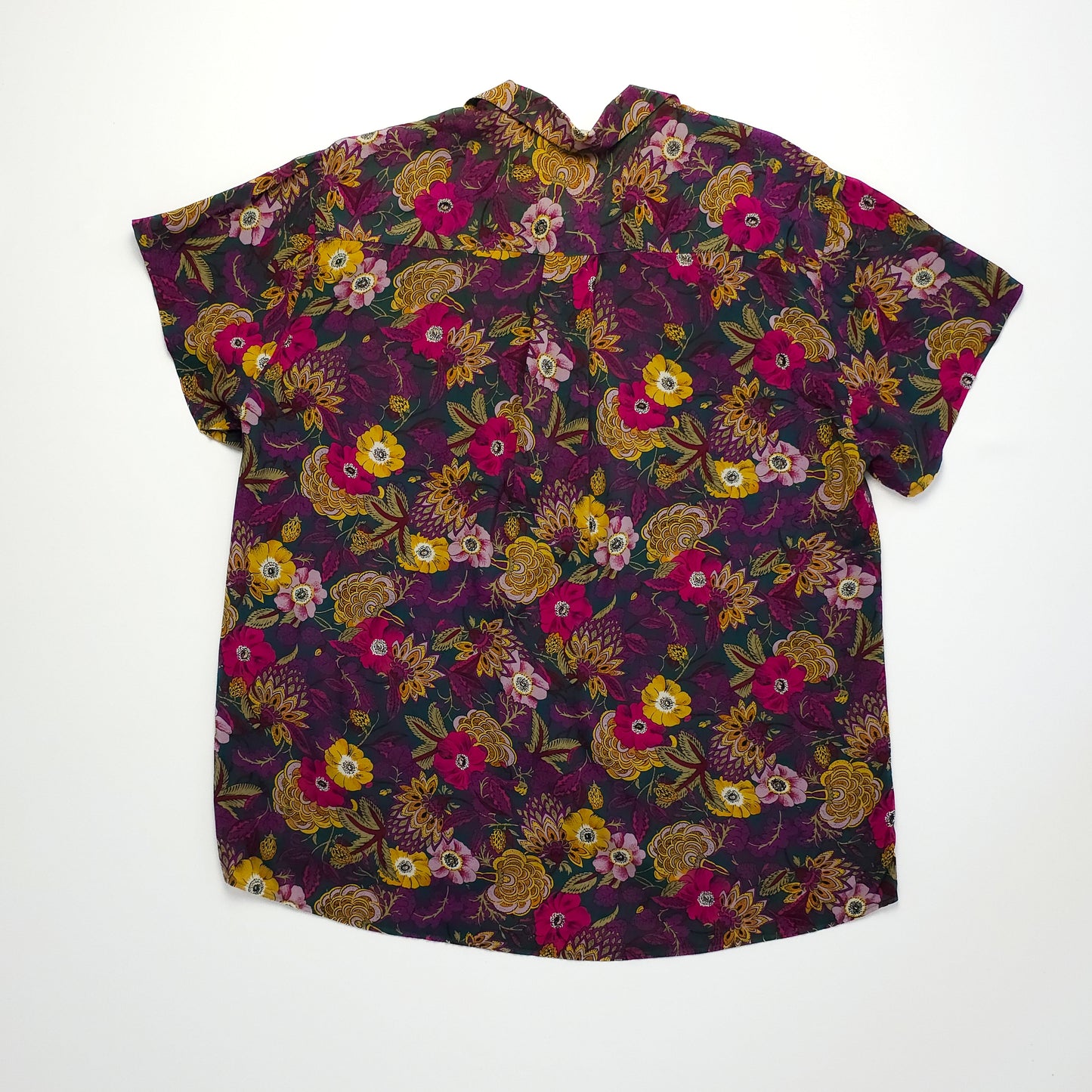 A short-sleeved blouse with a vibrant floral pattern in shades of pink, yellow, and purple on a dark background. The blouse has a loose fit and a back pleat.