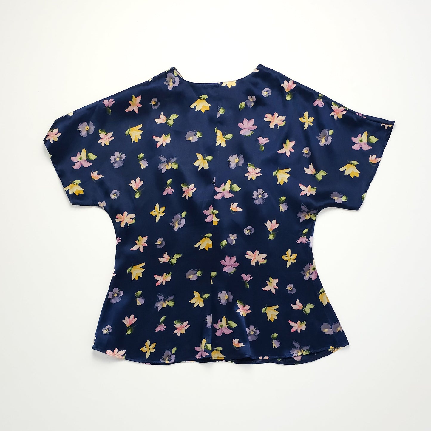 Navy blue satin blouse with short sleeves featuring a floral pattern of yellow, pink, and purple flowers. Relaxed fit with a slightly flared hem.