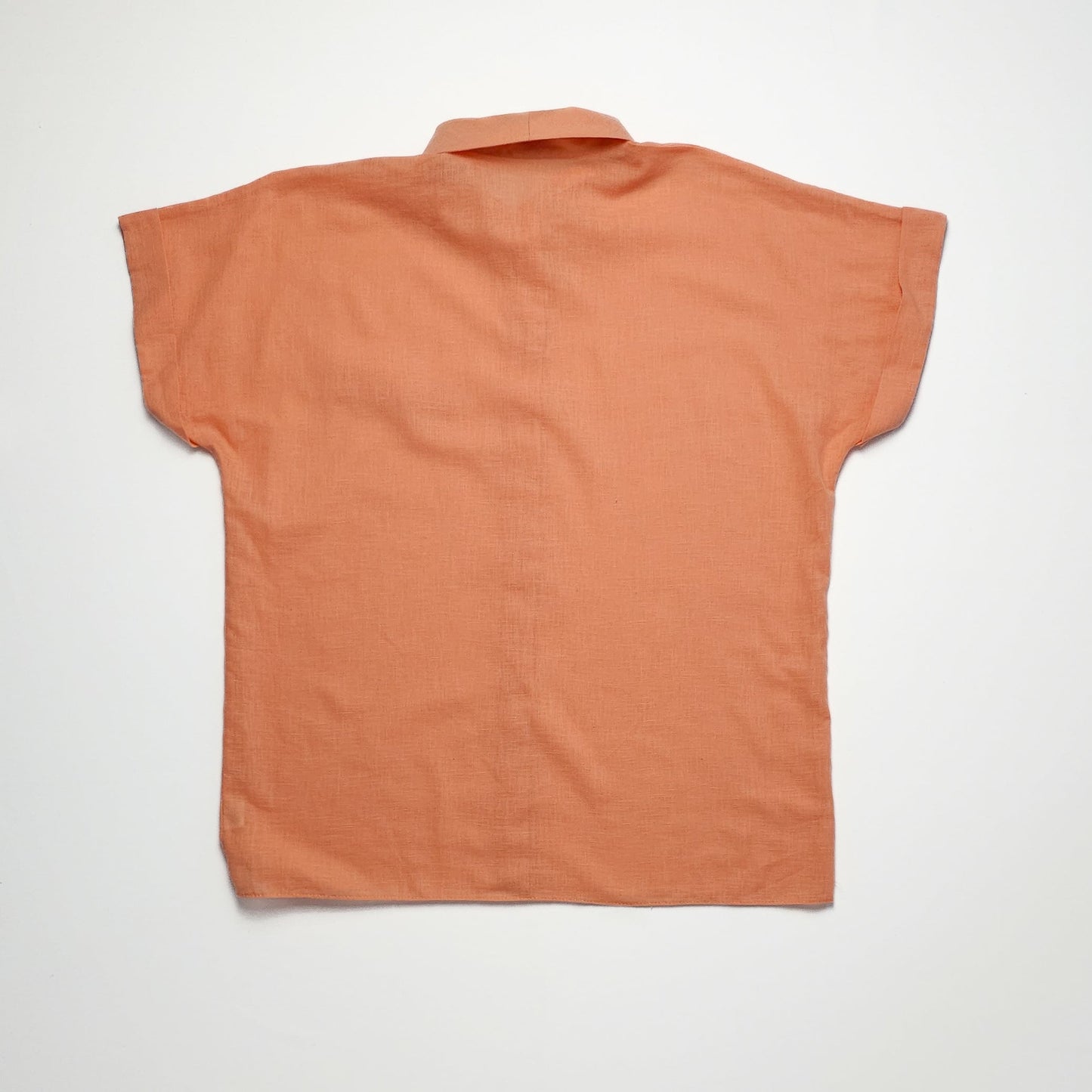 Back view of a short-sleeve, loose-fitting, light orange blouse with a small collar and a straight hem, displayed against a plain white background.