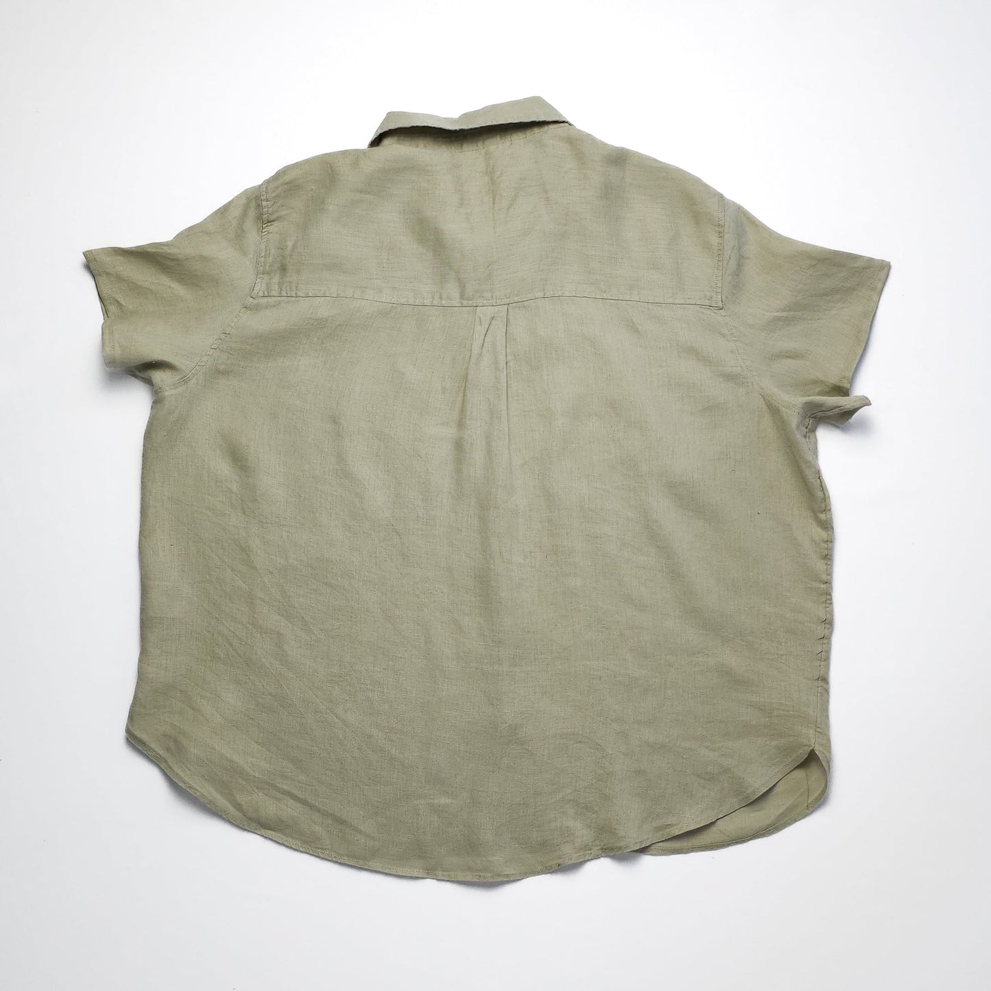 A short-sleeved, olive green button-up shirt is laid flat and viewed from the back. The fabric appears lightweight with a relaxed fit and a yoke seam.