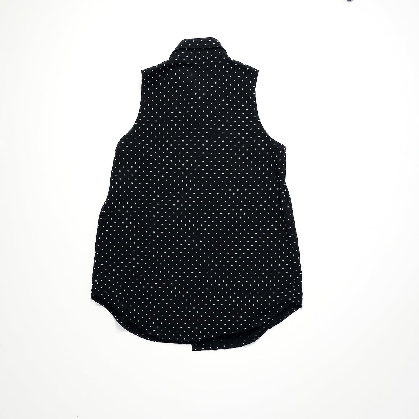 A sleeveless black blouse with white polka dots, featuring a collared neckline and an elongated hem at the back, displayed flat on a white background.