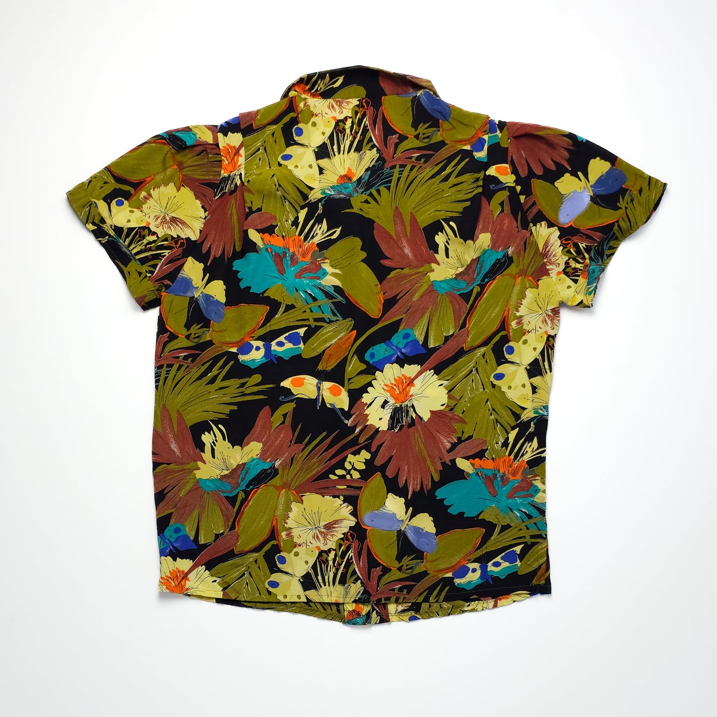 A short-sleeved button-up shirt featuring a vibrant tropical pattern with green leaves, colorful flowers, and abstract shapes on a dark background.