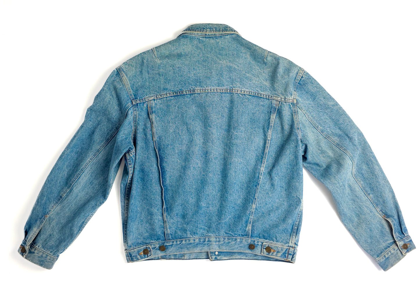A faded blue denim jacket with a classic design is laid flat, showcasing its back view. The jacket features button cuffs and a slightly worn appearance.