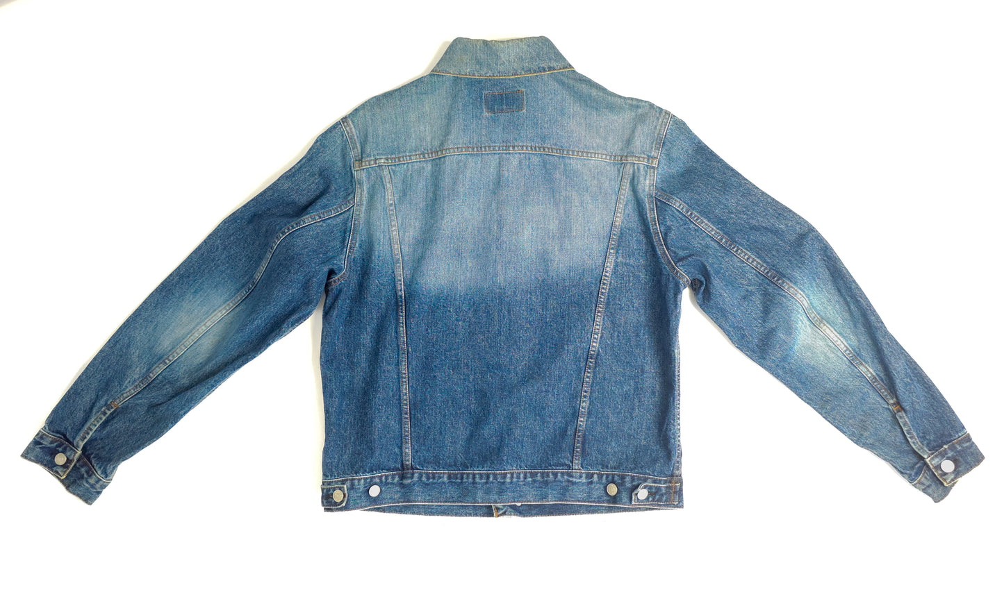 A faded blue denim jacket displayed on a white background. The jacket has long sleeves, buttoned cuffs, a pointed collar, and a stitched yoke.