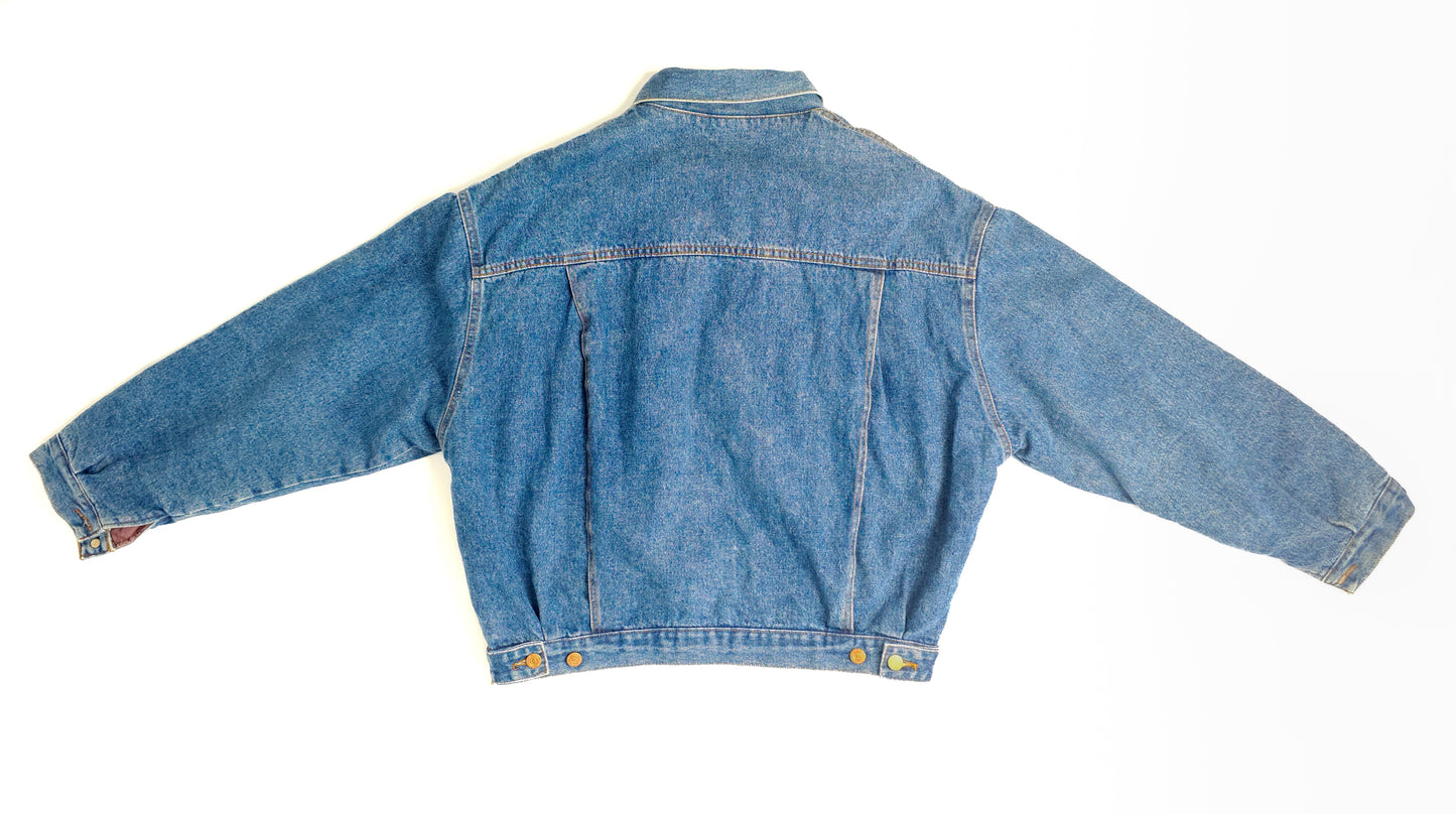 A classic vintage denim jacket with long sleeves, spread collar, and button details on the back. The jacket is laid flat on a white background.