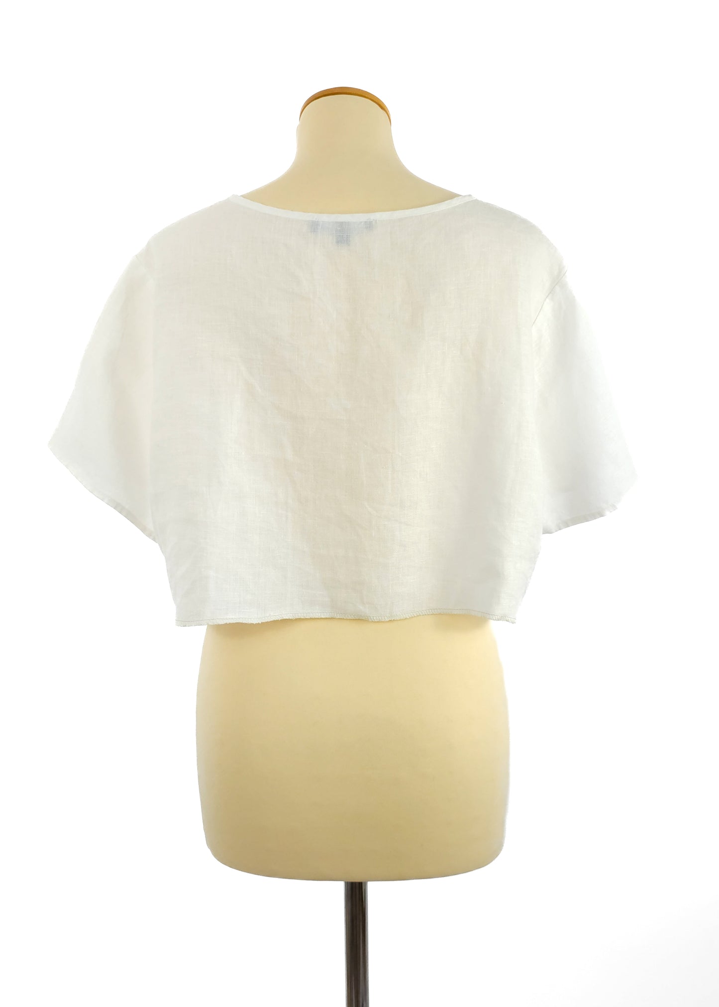 Back view of a white, short-sleeve, cropped linen top on a mannequin with a round neckline. The fabric has a loose, breathable texture.