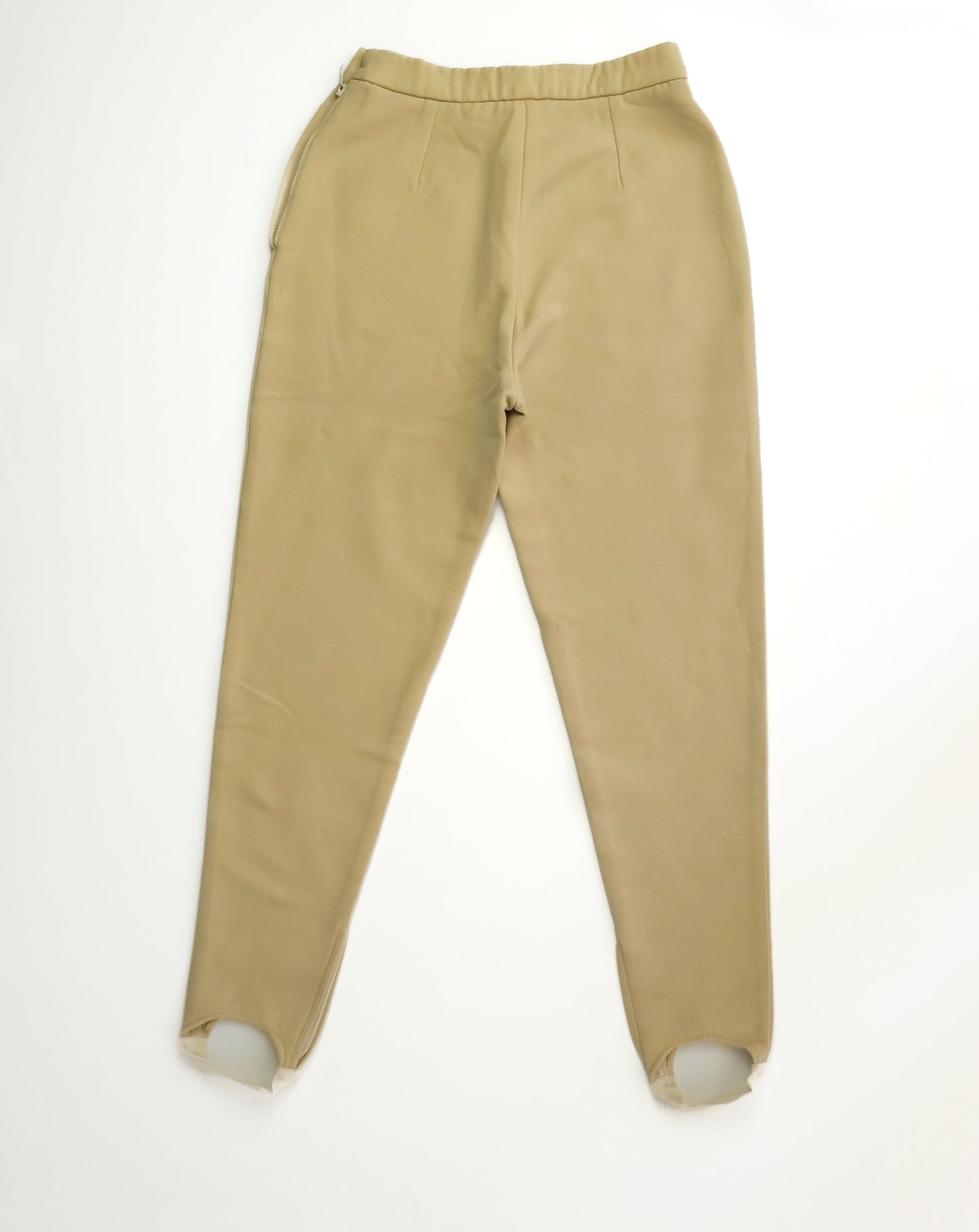 Beige high-waisted pants with elastic waistband, pleated front, and stirrups at the ankles, laid flat on a white background.