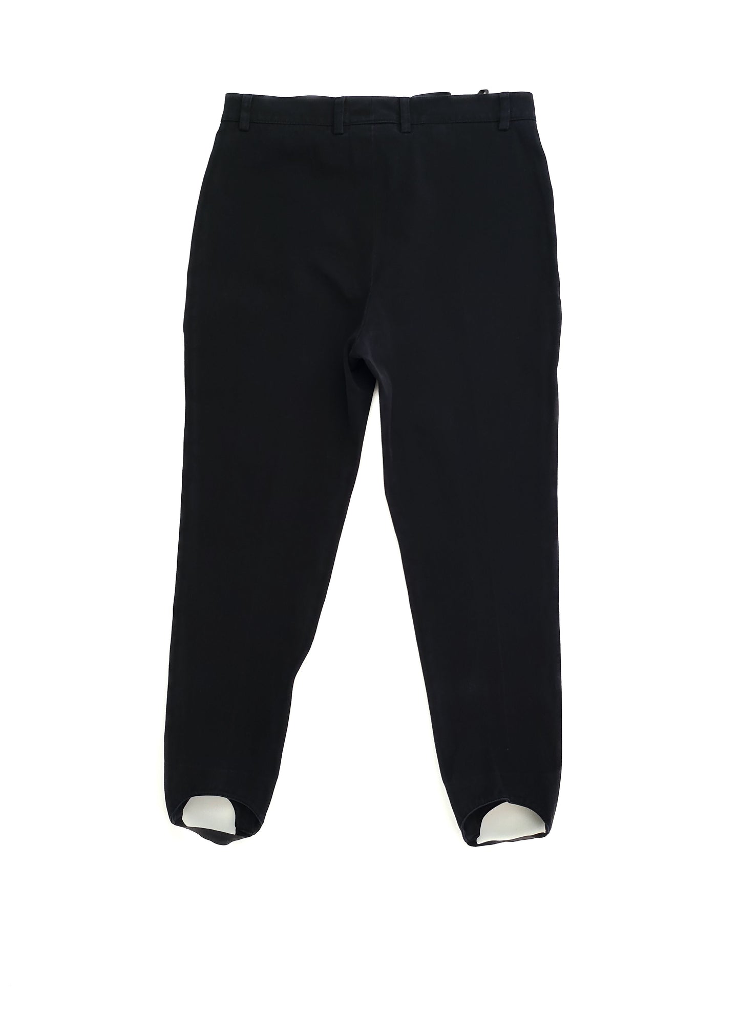 Black ankle-length pants with stirrups, designed for a snug fit. They have belt loops and a concealed side zipper closure, ideal for a sleek, modern look.
