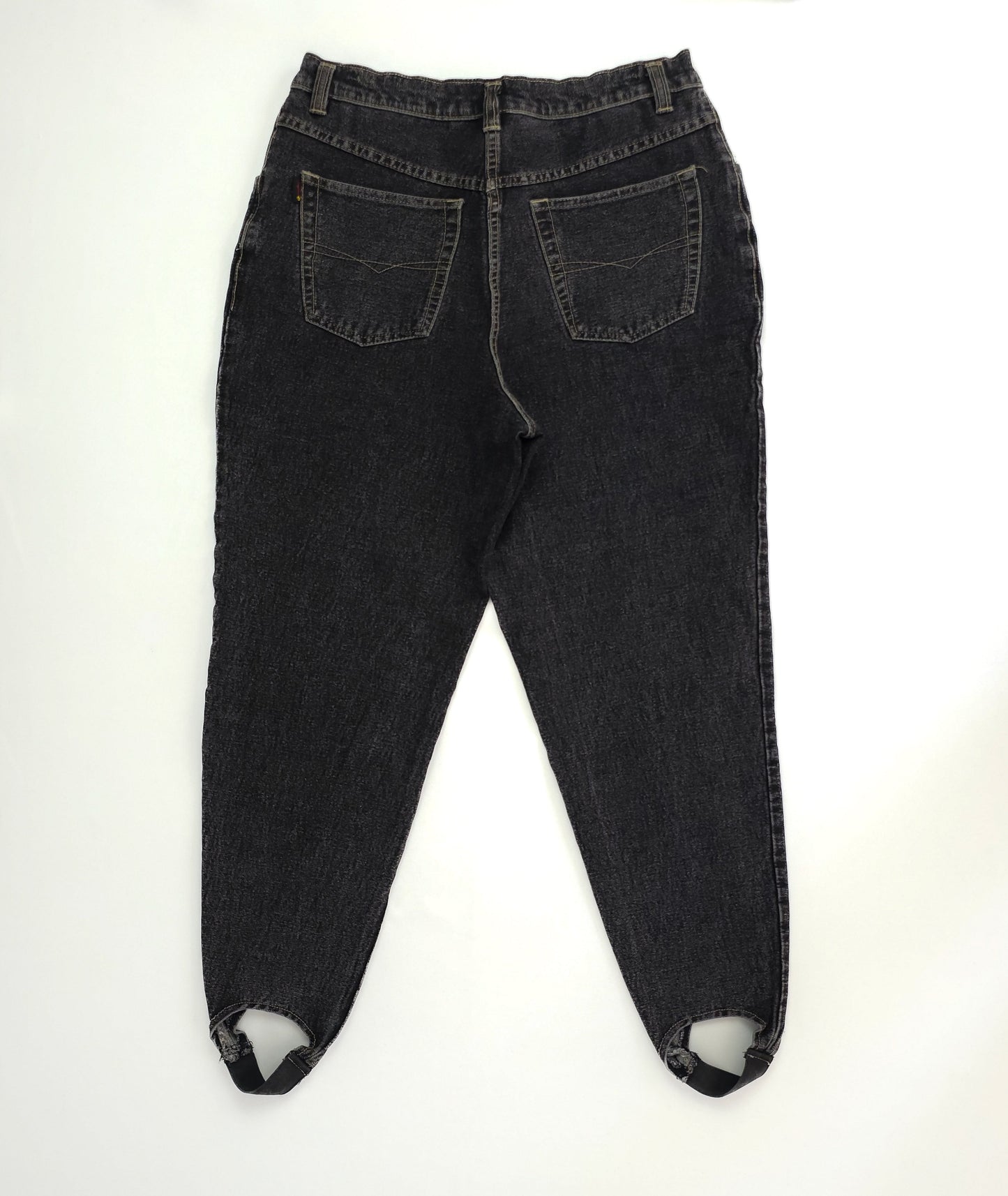 Black high-waisted denim jeans with back pockets and stirrup ankle straps, laid flat on a white background, showcasing a tapered fit and faded wash.