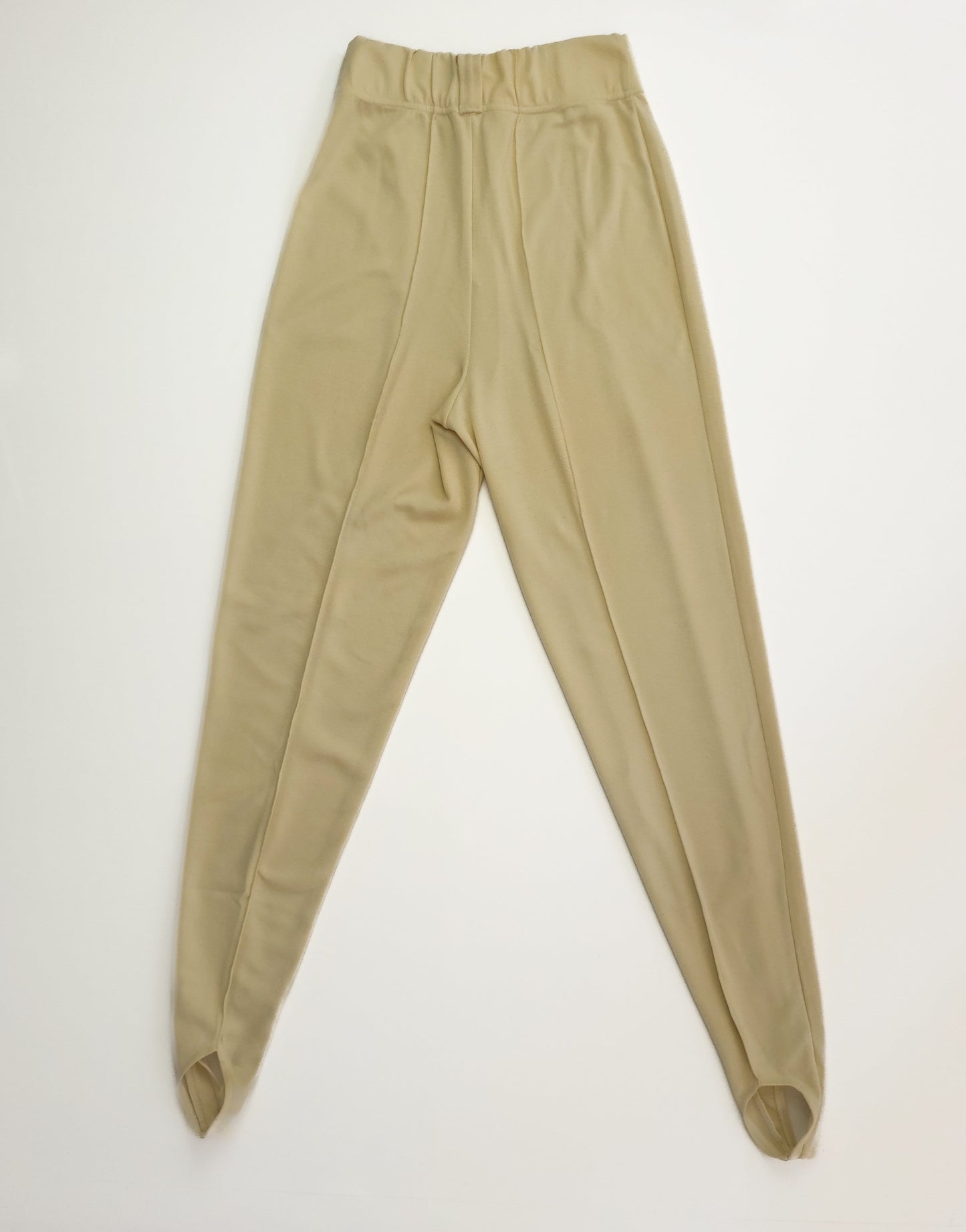 Beige high-waisted stirrup pants with a fitted design, displayed flat on a white background. The pants have an elastic waistband and are made of a stretchy fabric.