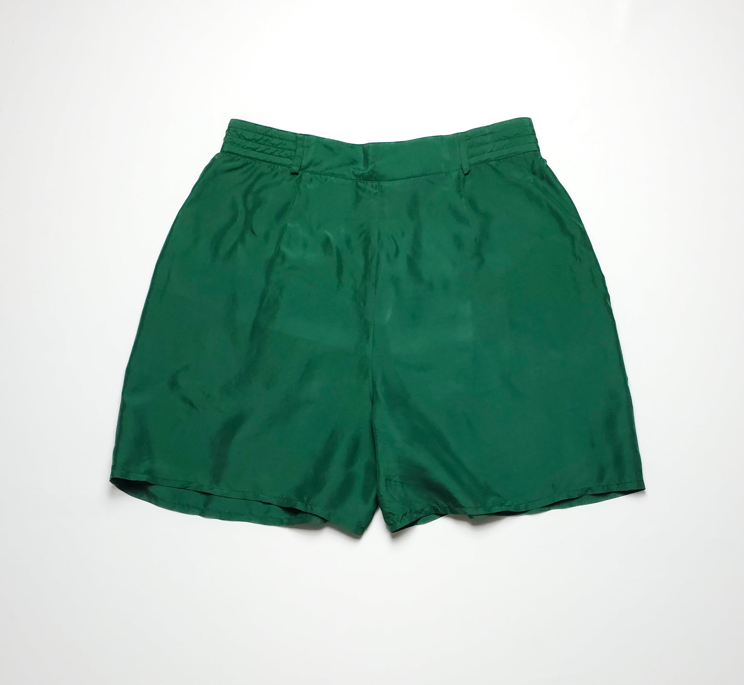 Green silk shorts with a high waist and loose fit, featuring a subtle sheen. The shorts have a simple design with belt loops and a hem above the knee.
