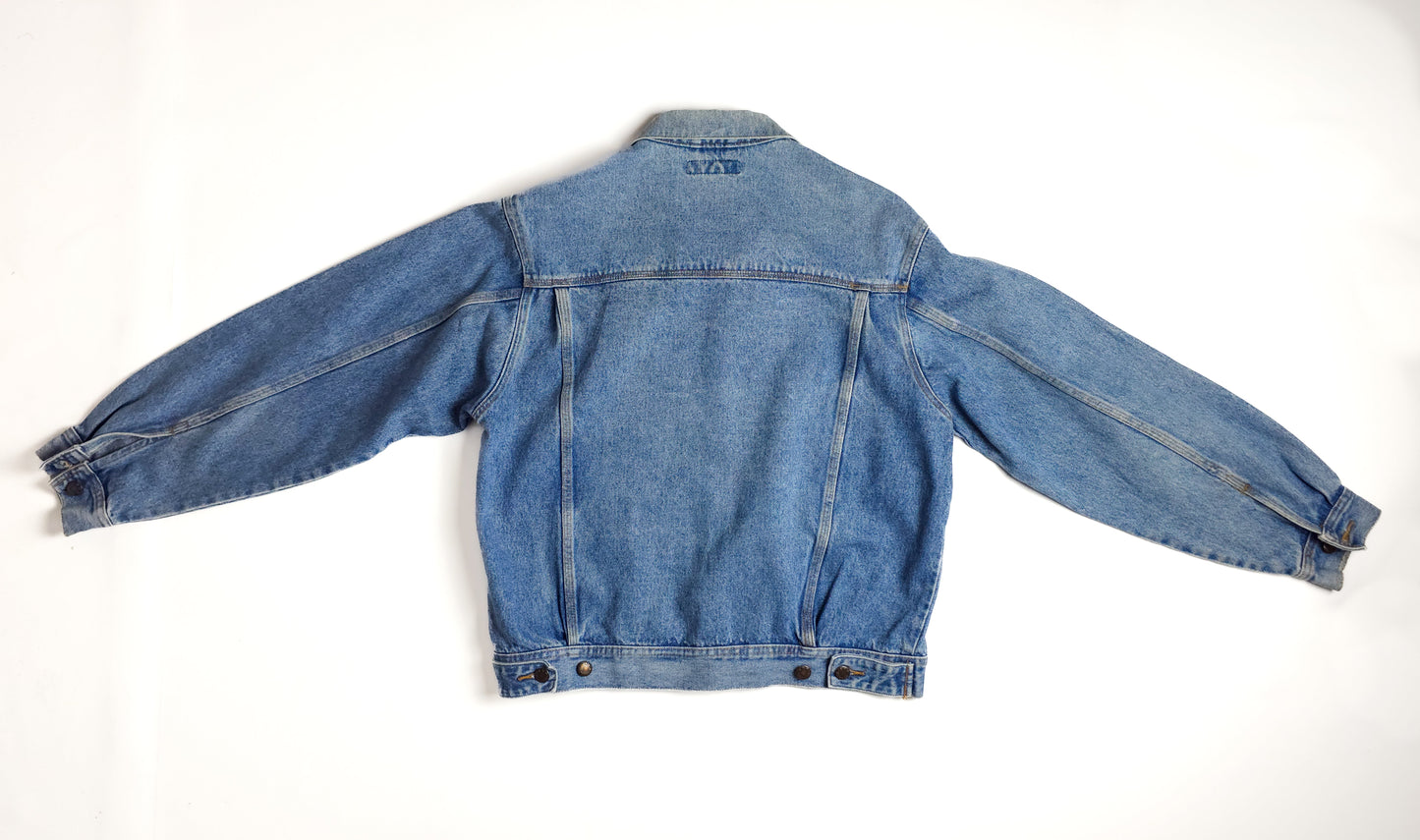 Blue denim jacket with long sleeves, buttoned cuffs, and a slightly faded, worn-in look. The jacket is laid flat, back facing up on a white background.