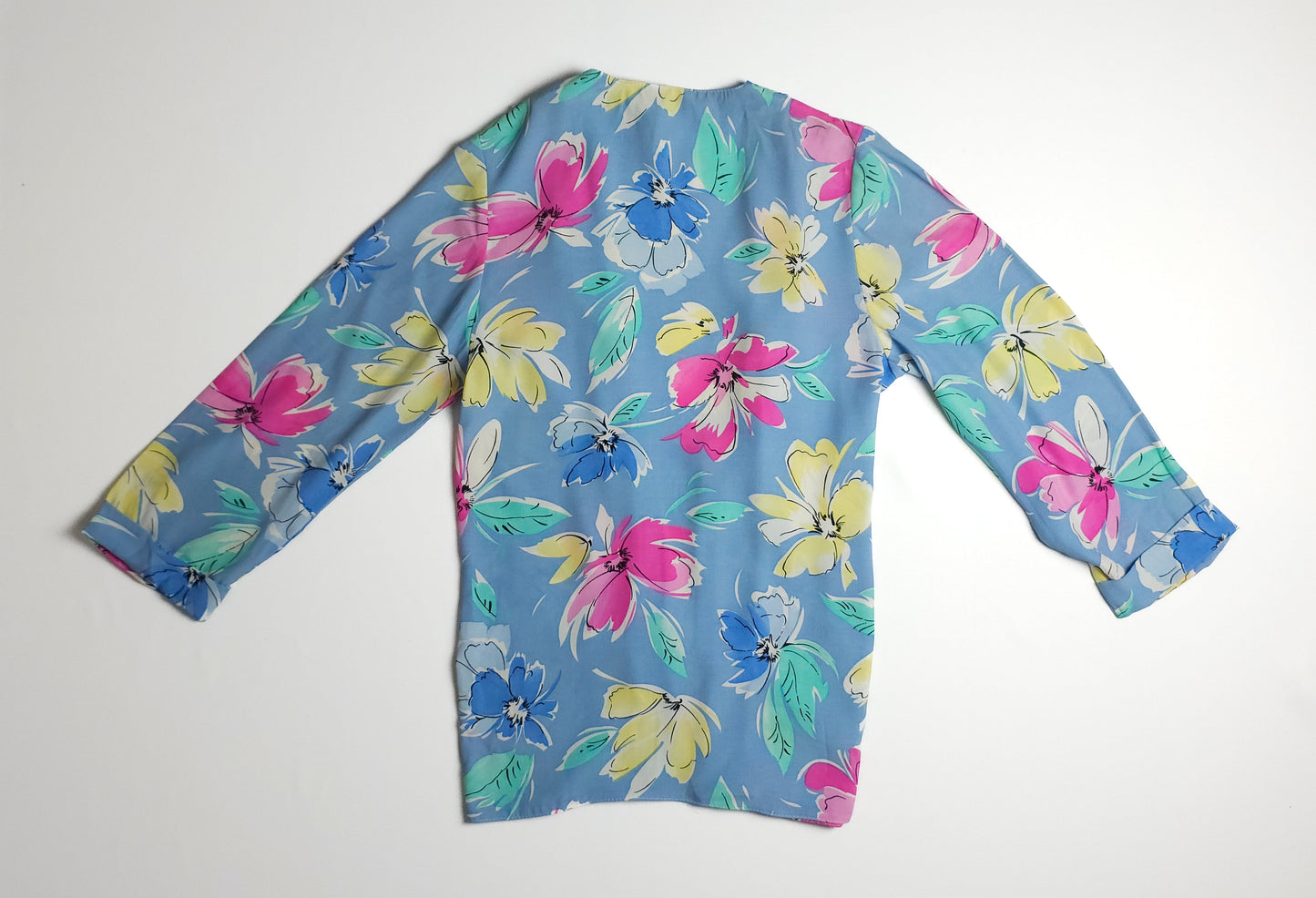 Long-sleeved top with colorful floral print on a light blue background. Features pink, yellow, green, and blue flowers with a loose and casual fit.