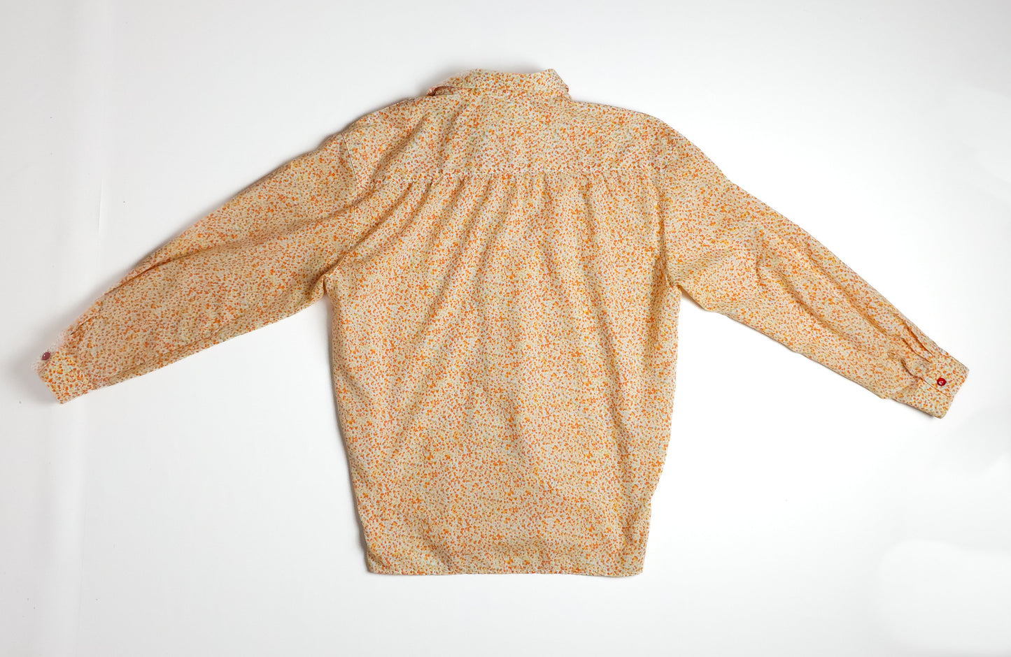 A vintage long-sleeve blouse in a light beige color with a colorful floral print, featuring a button-up design and gathered details at the shoulders.