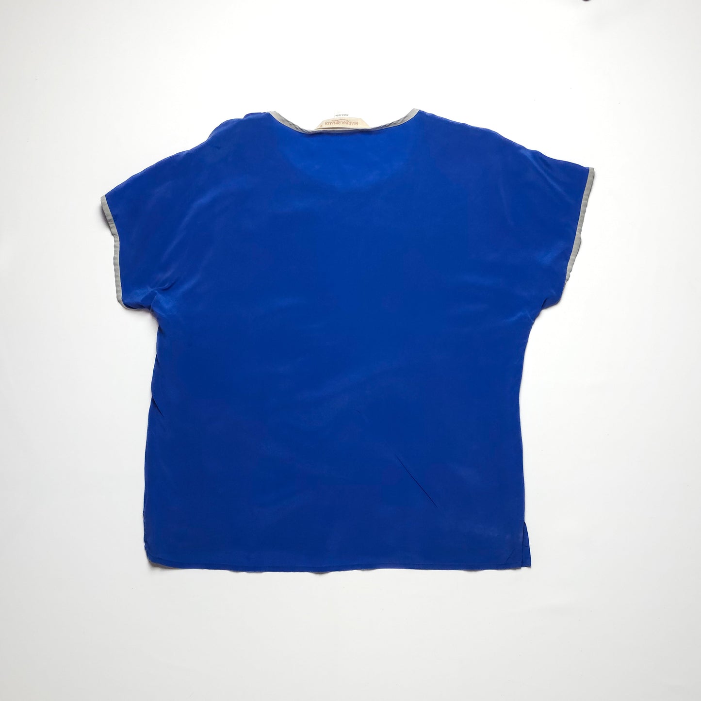 A vibrant blue short-sleeved blouse with a loose fit, featuring contrasting light gray trim on the sleeves and neckline. The blouse is laid flat on a white background.