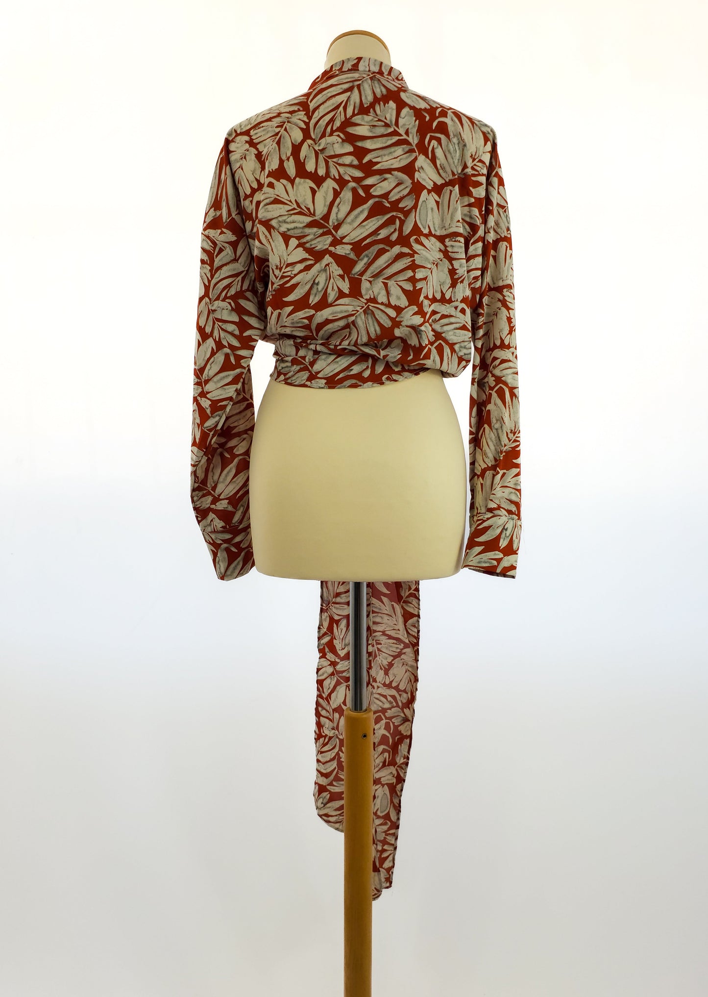 Rear view of a long-sleeved shirt with a red and white leaf pattern on a mannequin. The shirt features a unique elongated back detail.