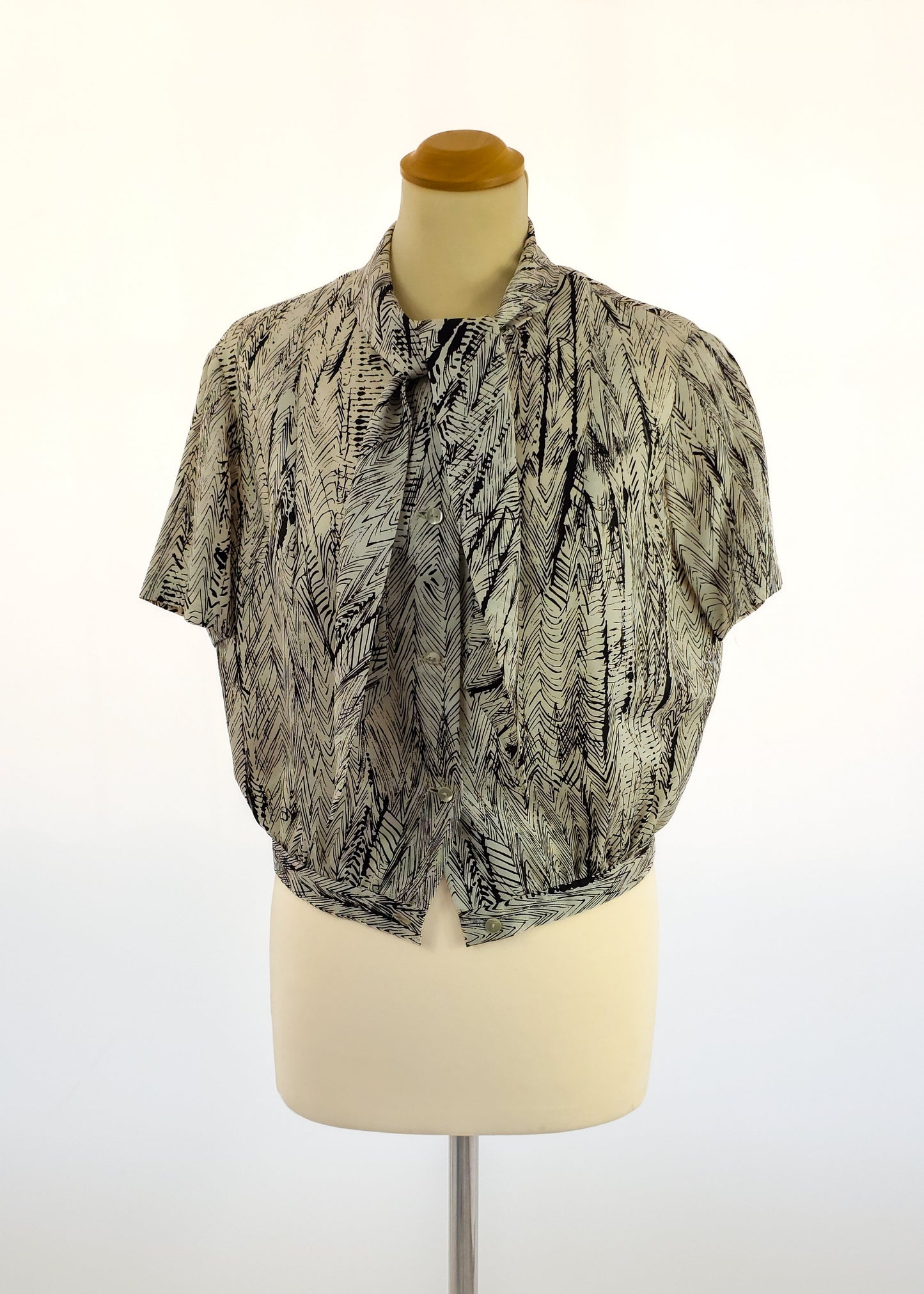 Short-sleeved blouse with a vintage feather-like pattern in black and gray on a white background, displayed on a mannequin, featuring a gathered neckline.