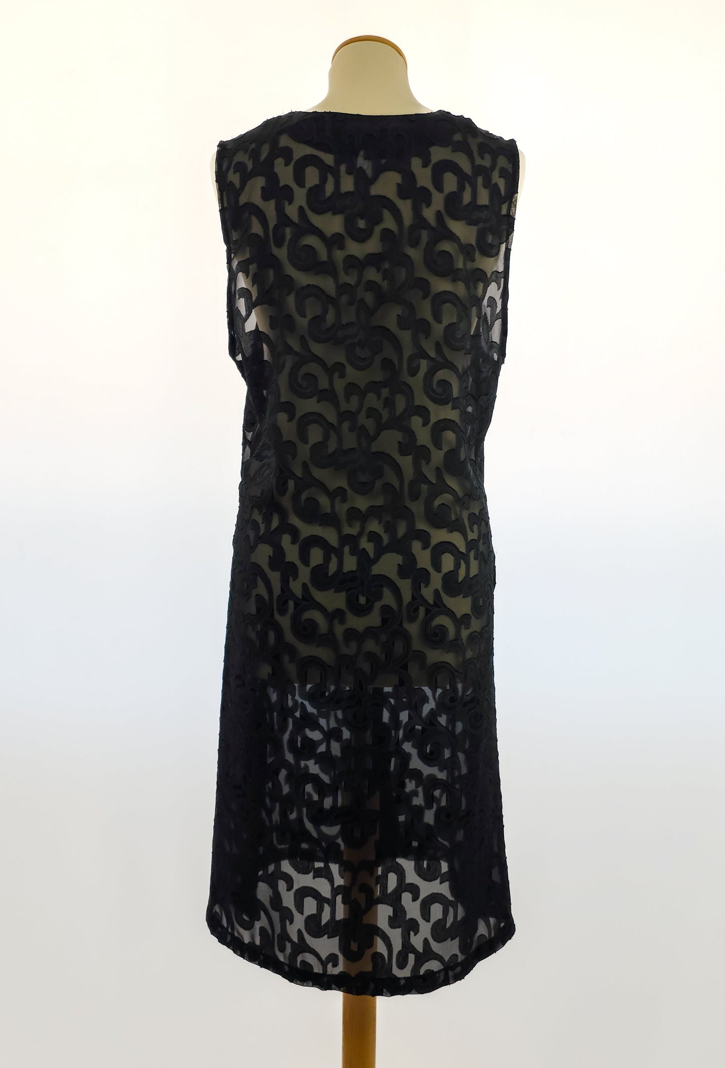 A sleeveless black lace dress on a mannequin, featuring an intricate floral pattern and a knee-length hemline. The background is plain white.